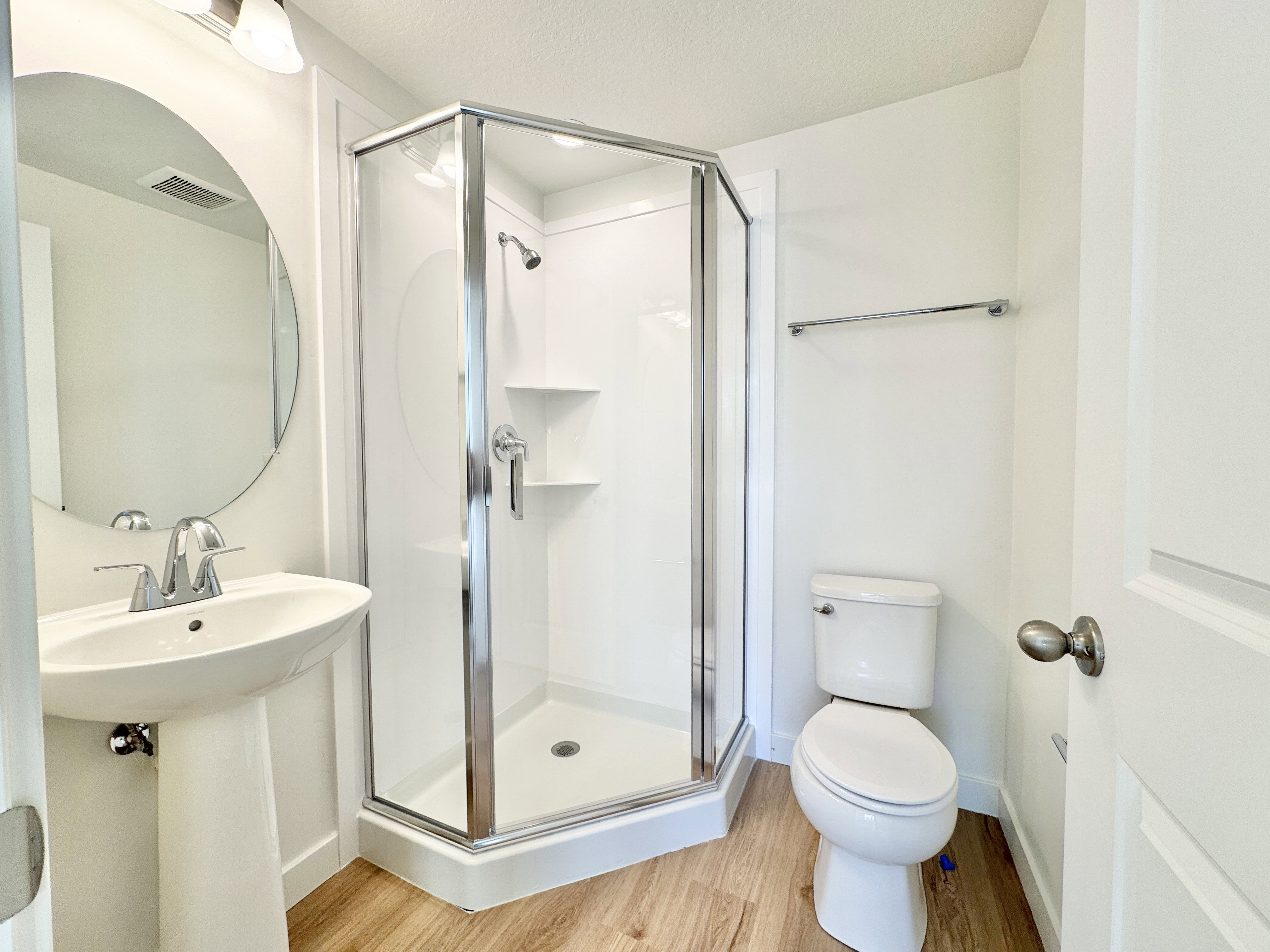 Full bathroom featuring a glass-enclosed shower with chrome fixtures, a pedestal sink, and wood-finish flooring