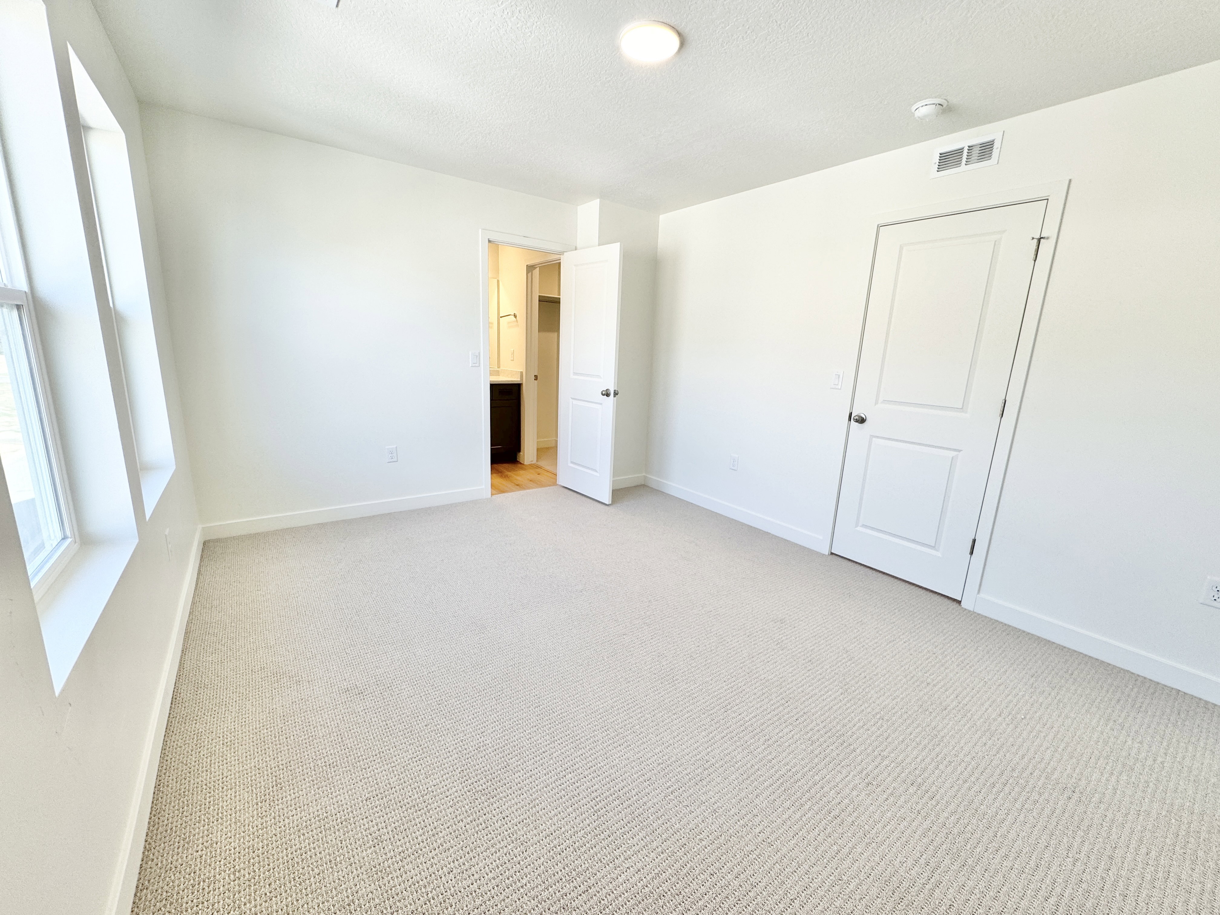 Neutral-toned carpeting extends throughout this room, featuring multiple windows and bright white walls