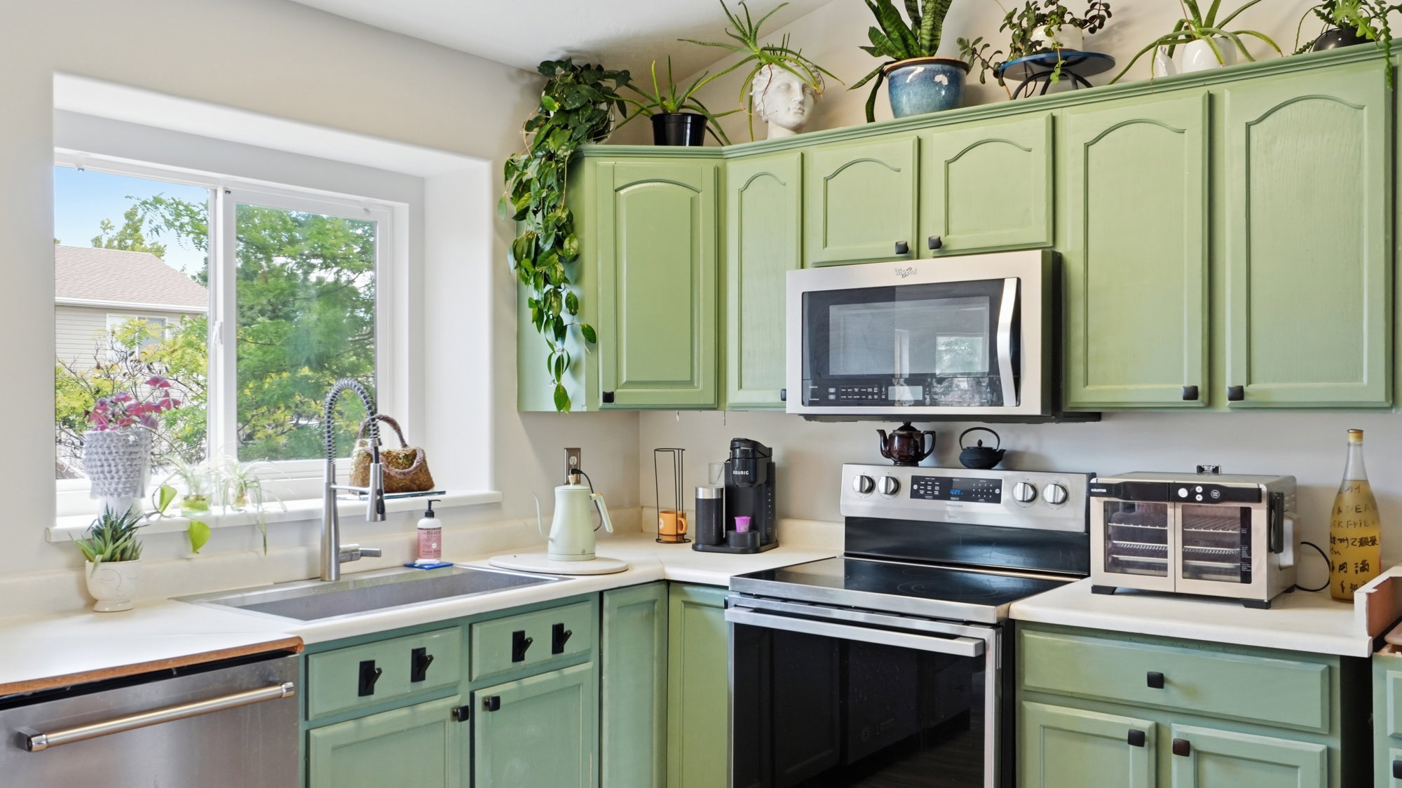 Kitchen featuring light green cabinetry with black hardware, white countertops, and stainless steel appliances