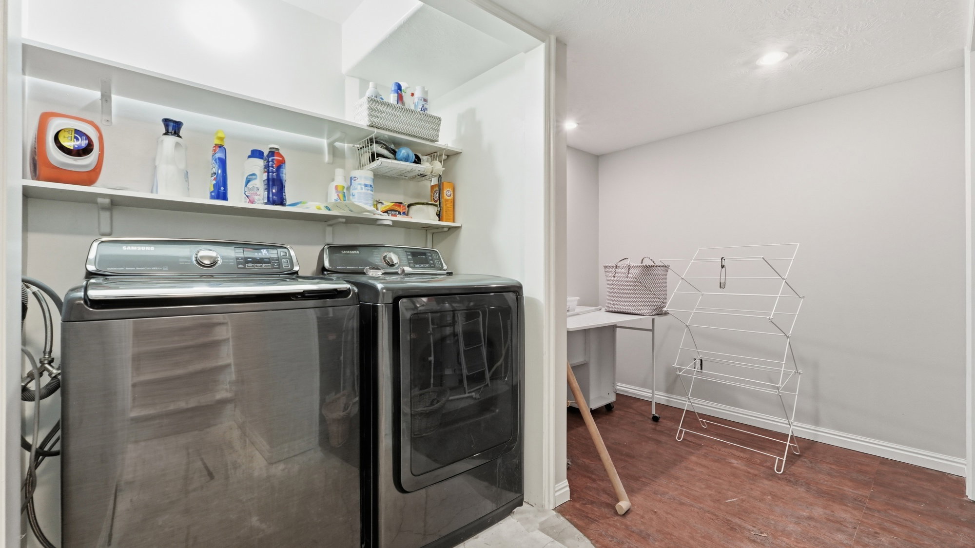 Dedicated laundry area featuring a washer and dryer, wall-mounted shelving for storage, and wood-finish flooring