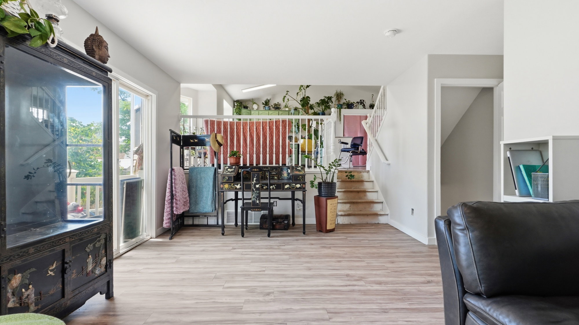 Spacious open-concept interior featuring light wood-finish flooring, a white-painted stairwell, and a built-in wall shelf