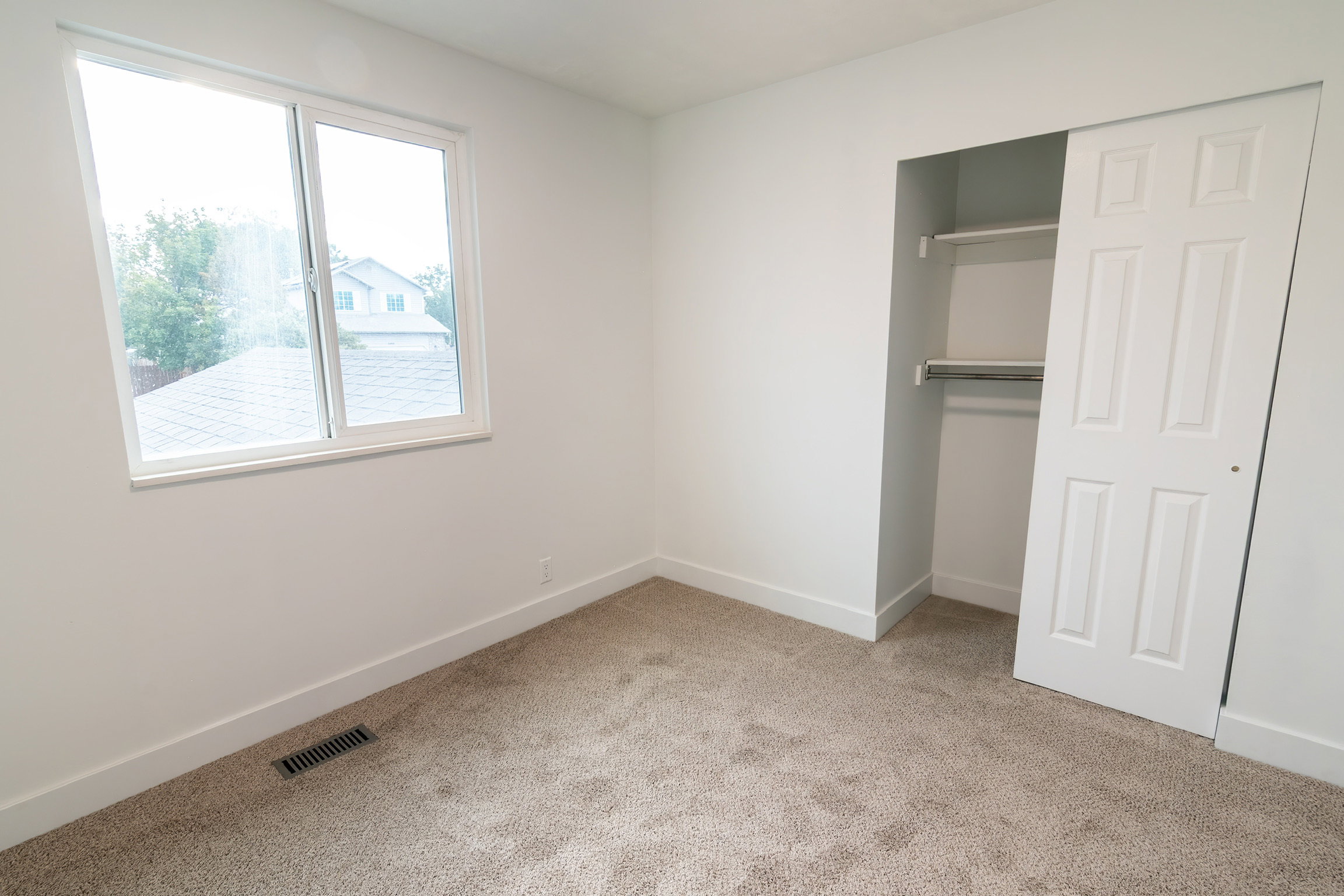 Bedroom featuring a large window, neutral carpeting, white walls, and a closet with sliding paneled doors