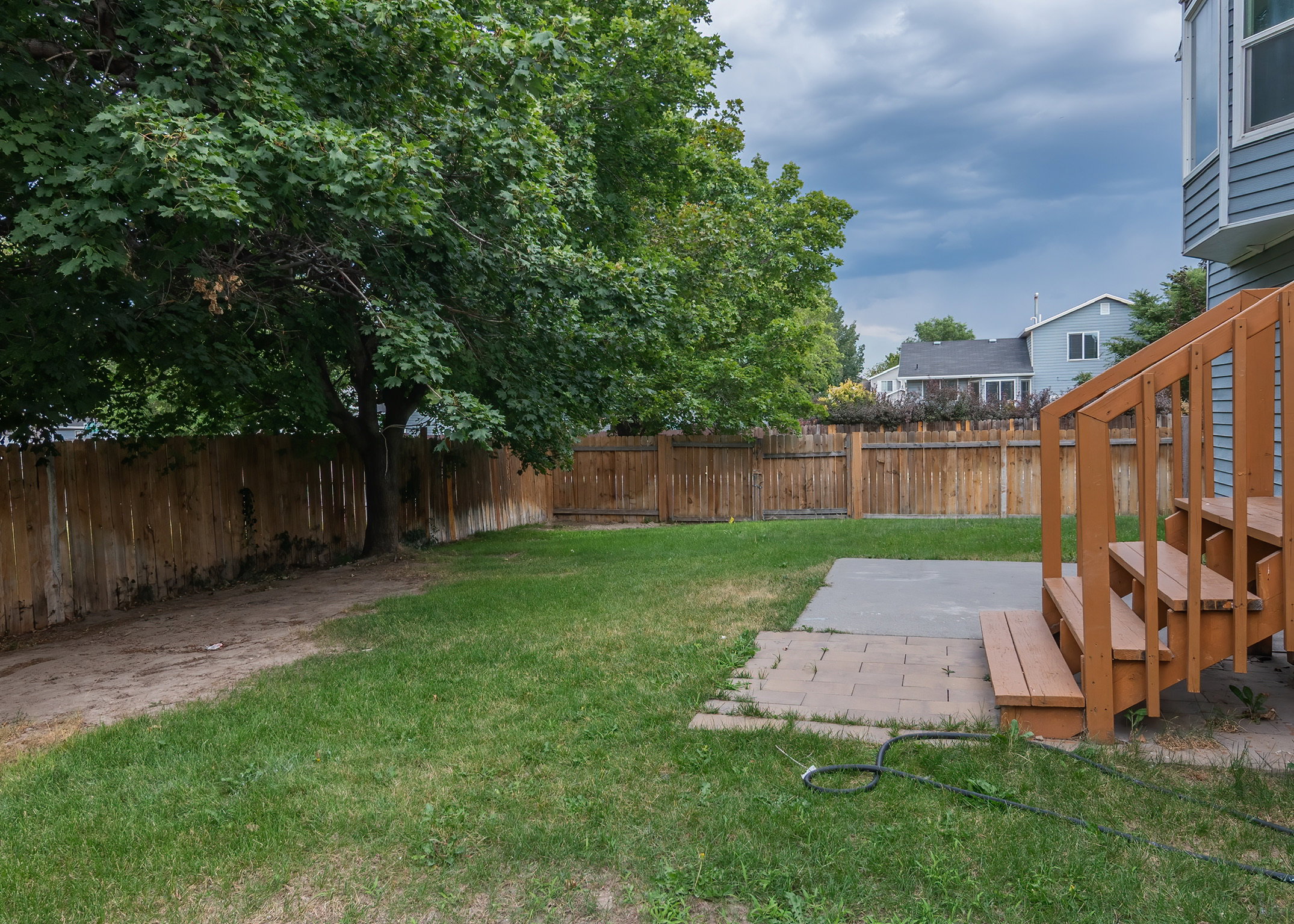 Expansive backyard featuring a manicured lawn, established trees, and a full privacy fence