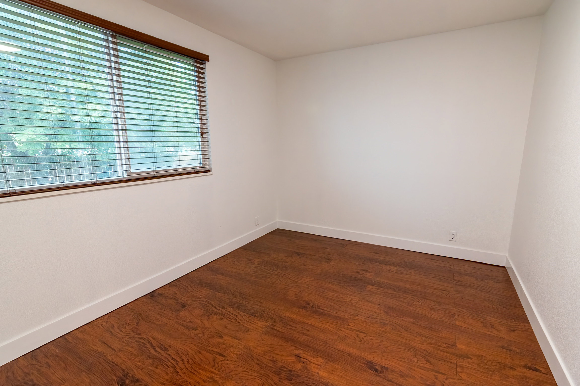 Bright room featuring wood-finish flooring, white walls, and a window with wood blinds