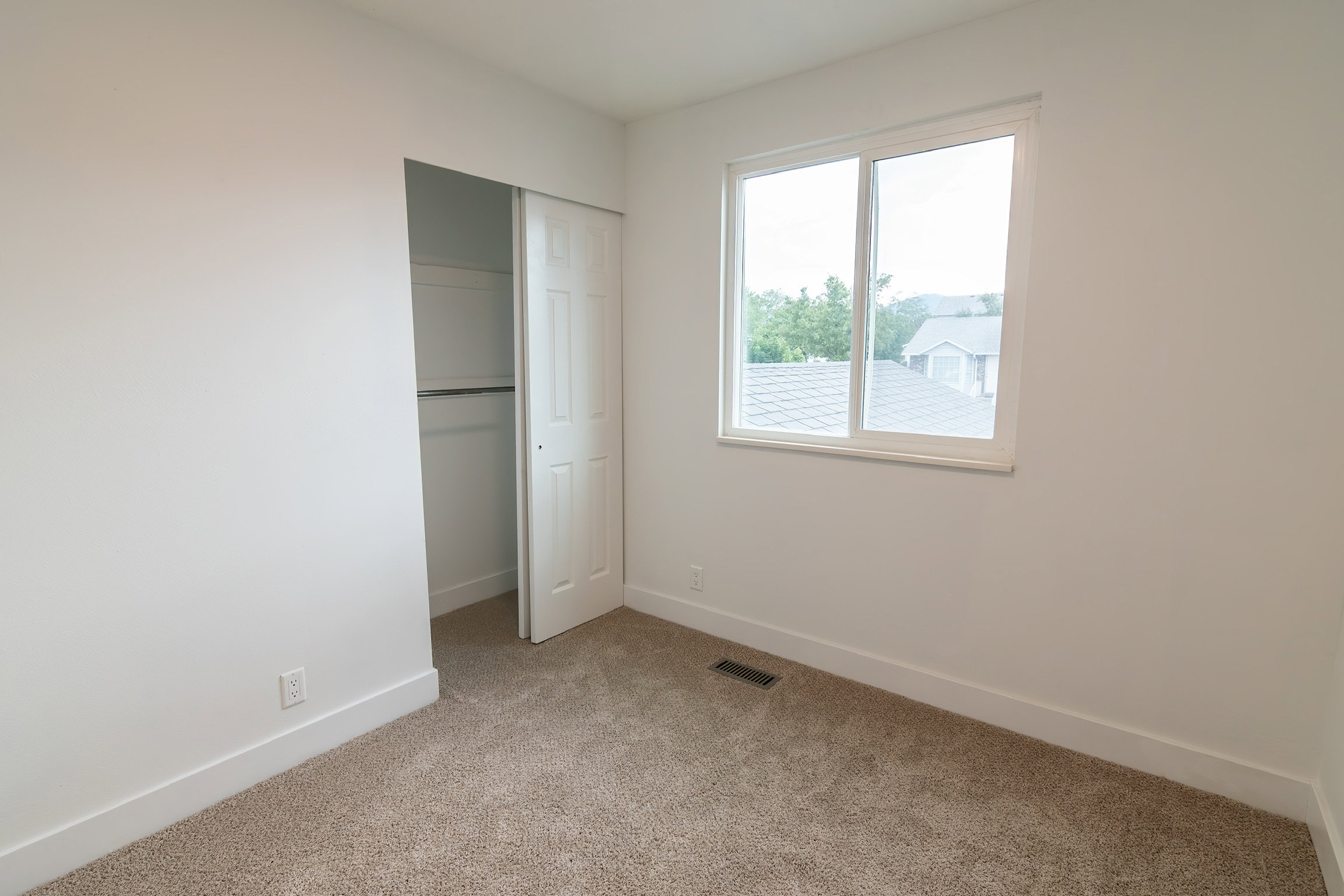 Carpeted room featuring a double-paned window, white trim, and a bi-fold door closet with shelving and hanging rod