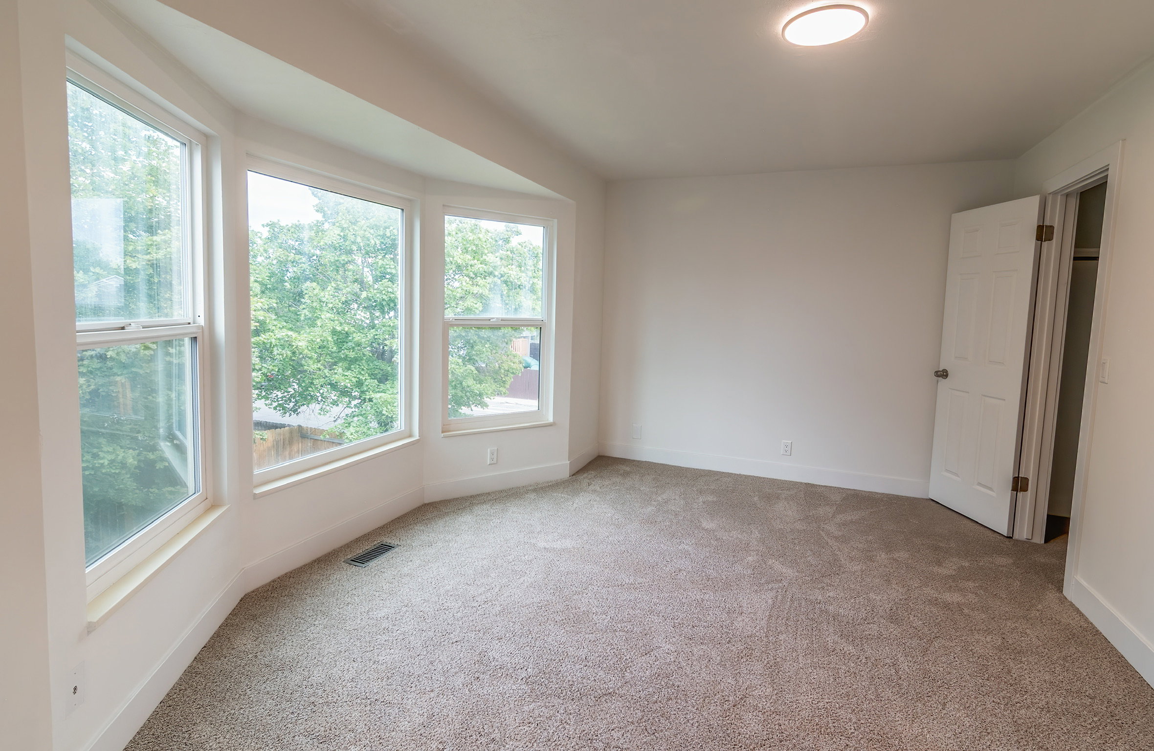 Room featuring a three-panel bay window, neutral carpeting, white walls, and a flush-mount ceiling light fixture