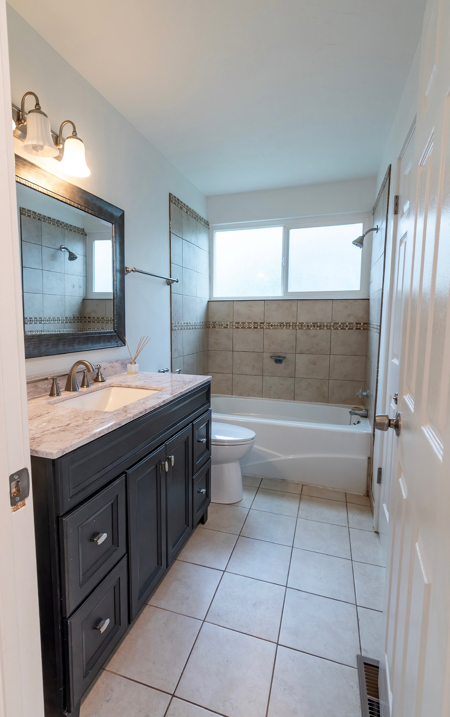 Bathroom featuring a dark wood vanity with a light-toned countertop, a tile floor, a shower-tub combination with tiled surround, and a window with frosted glass
