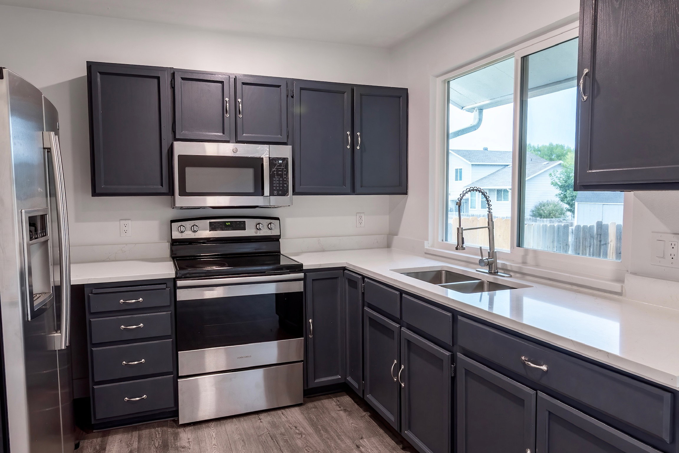 Contemporary kitchen featuring dark cabinetry with brushed nickel hardware, white countertops, and stainless steel appliances