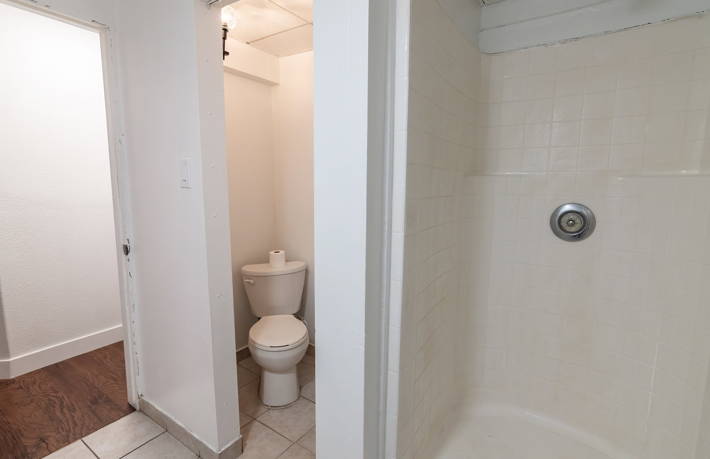 Three-piece bathroom featuring a shower stall with tiled walls, a standard toilet, and tiled flooring