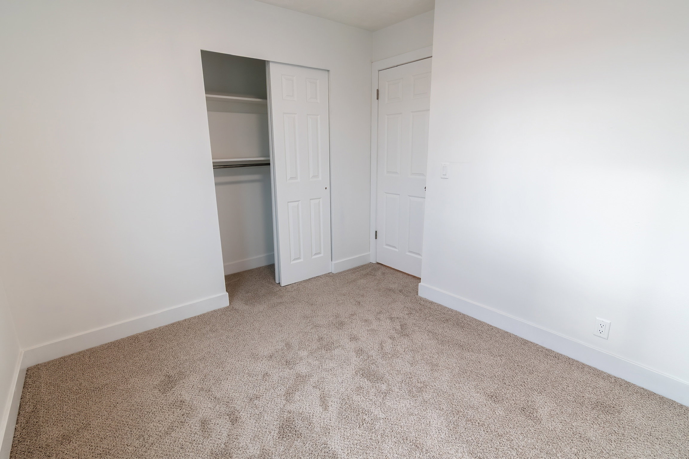 Neutral tone carpeted room featuring white walls and a white baseboard trim