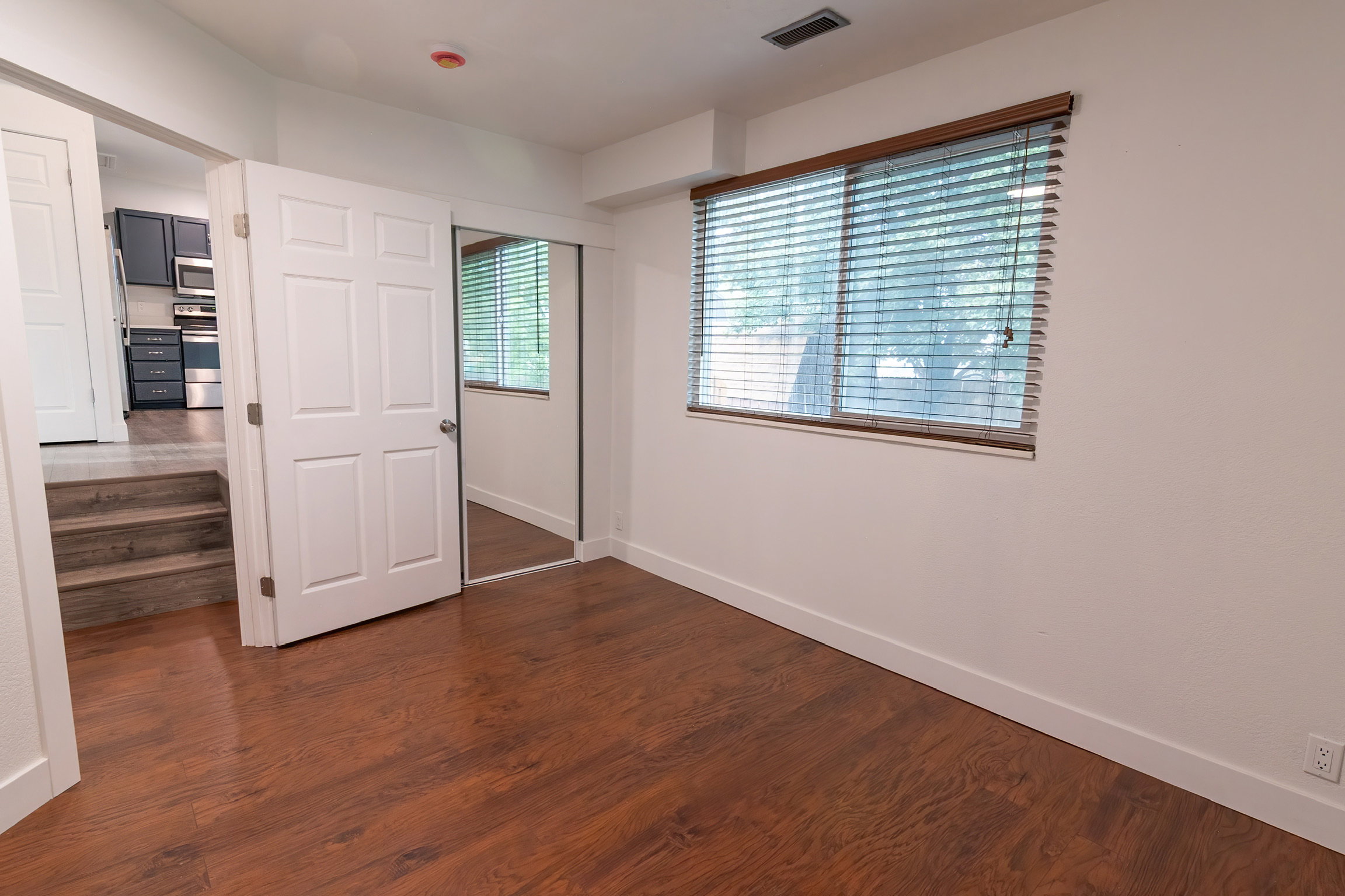 Room featuring wood-finish flooring, a window with horizontal blinds, and a mirrored closet door