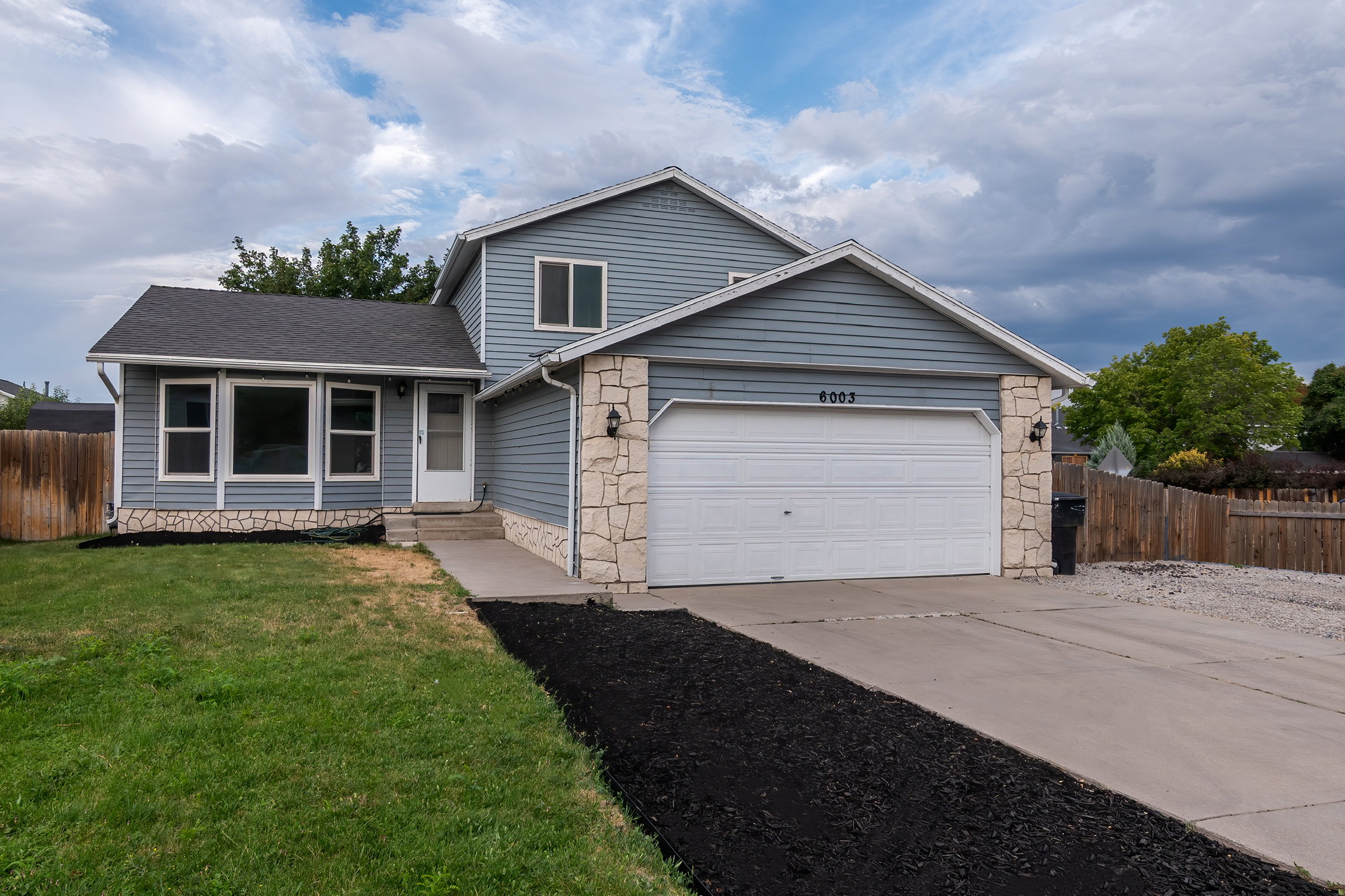 Two-story residence featuring blue siding, stone facade accents, and a two-car garage