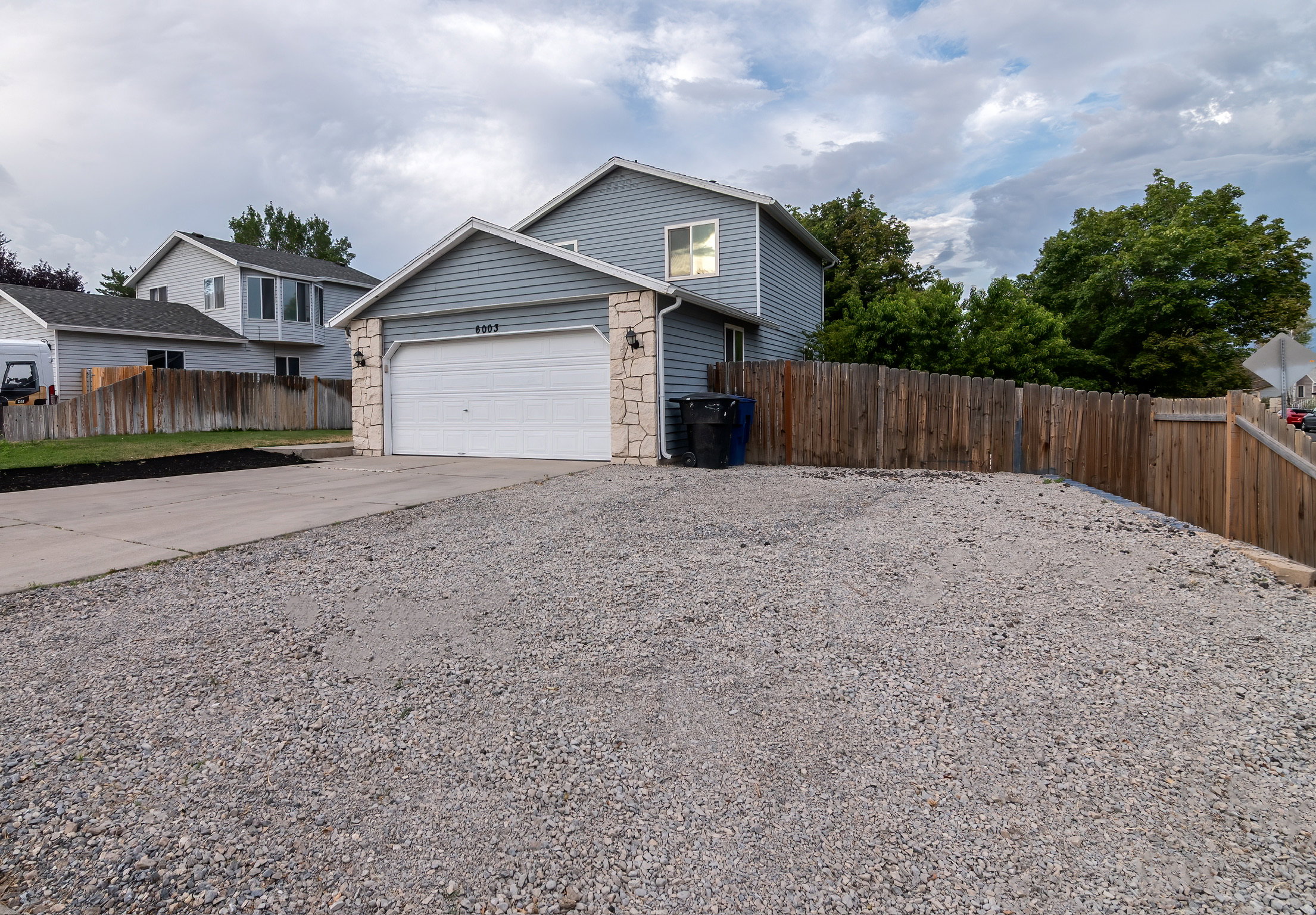 Exterior featuring light blue siding, a two-car garage with white door, stone veneer accents, and exterior wall lanterns