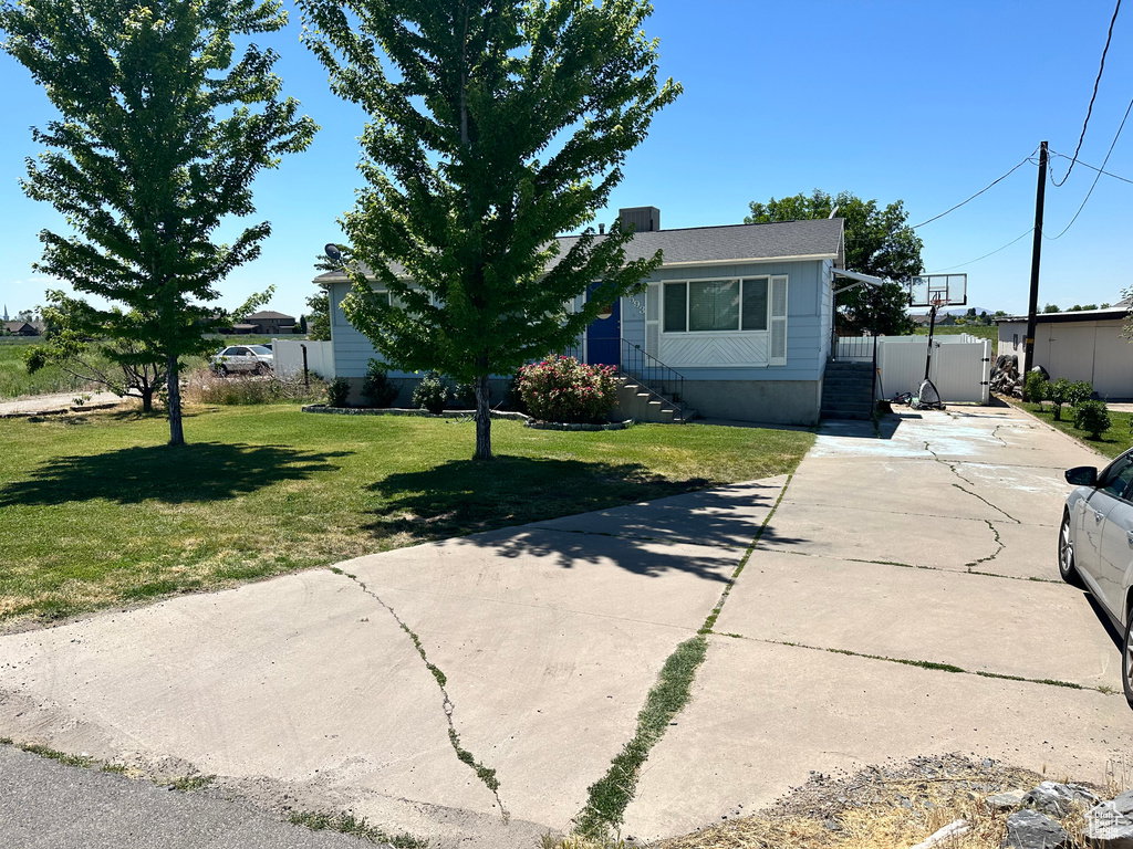 Light blue exterior with white trim, featuring a concrete driveway, a green lawn, and two mature deciduous trees