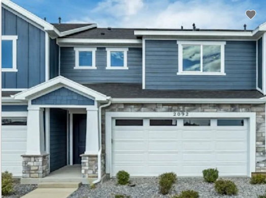 Modern townhome exterior featuring blue horizontal siding, a stone veneer facade, a covered entry with stone-clad columns, a two-car garage with transom windows, and white trim accents. This home is under construction, and pictures are of a similar home.
