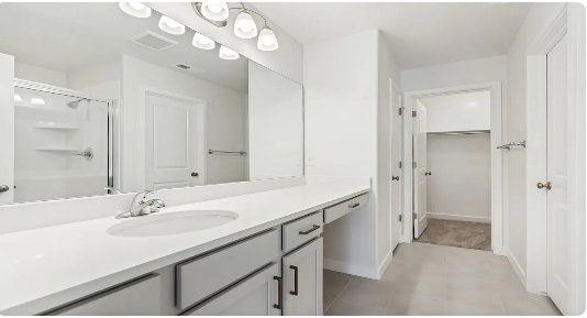 Dual-sink vanity with white countertop, chrome fixtures, and integrated mirror. This home is under construction, the pictures are of a similar home