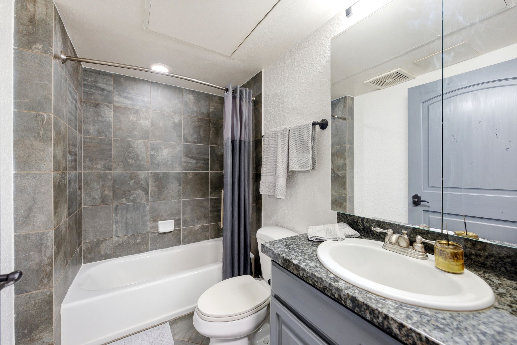 Bathroom featuring a tub/shower combination with tile surround, a vanity with a granite-style countertop, an oval undermount sink, and a framed mirror