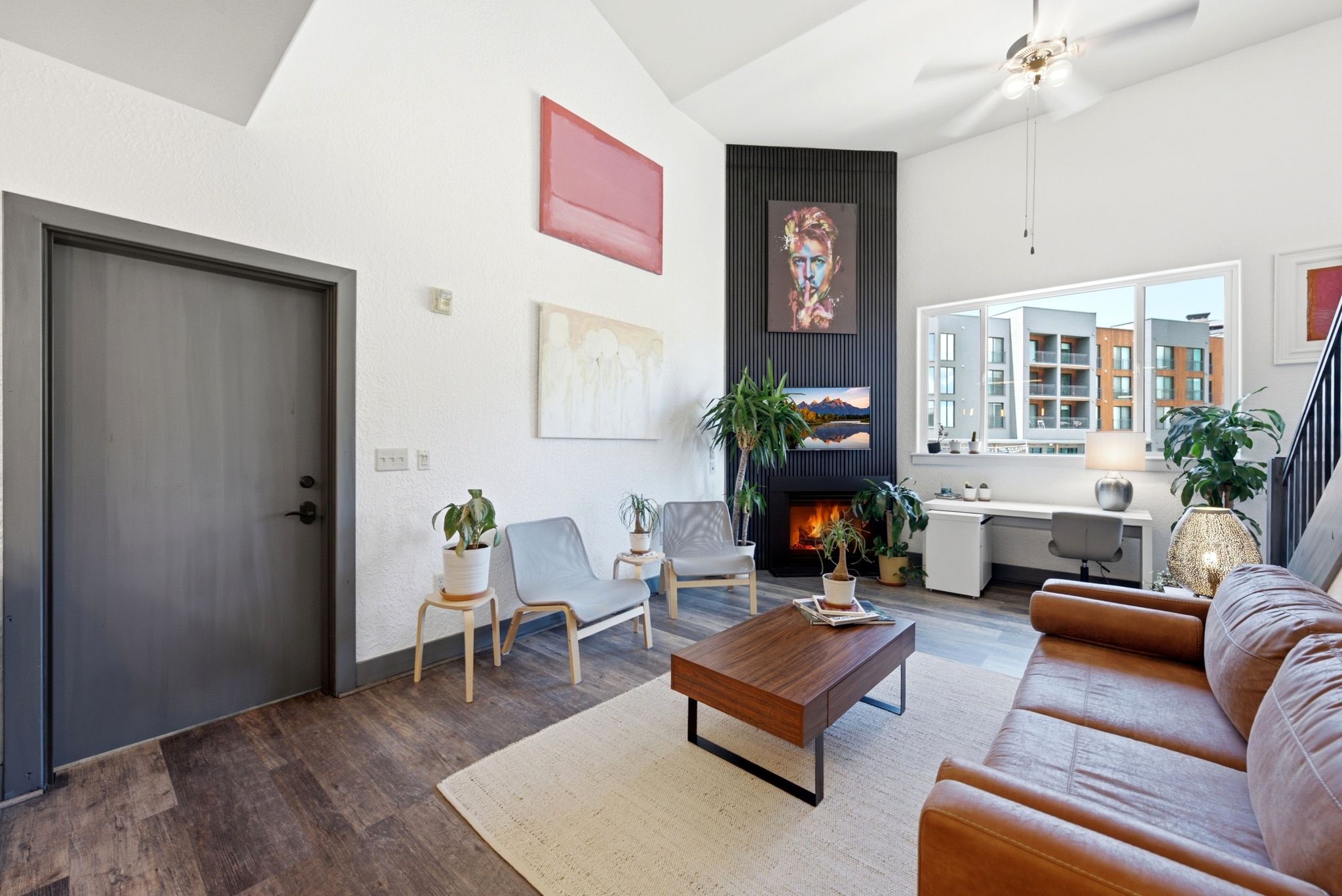 Living area featuring a vaulted ceiling with a ceiling fan, wood-finish flooring, a built-in fireplace, a built-in desk, and a large window