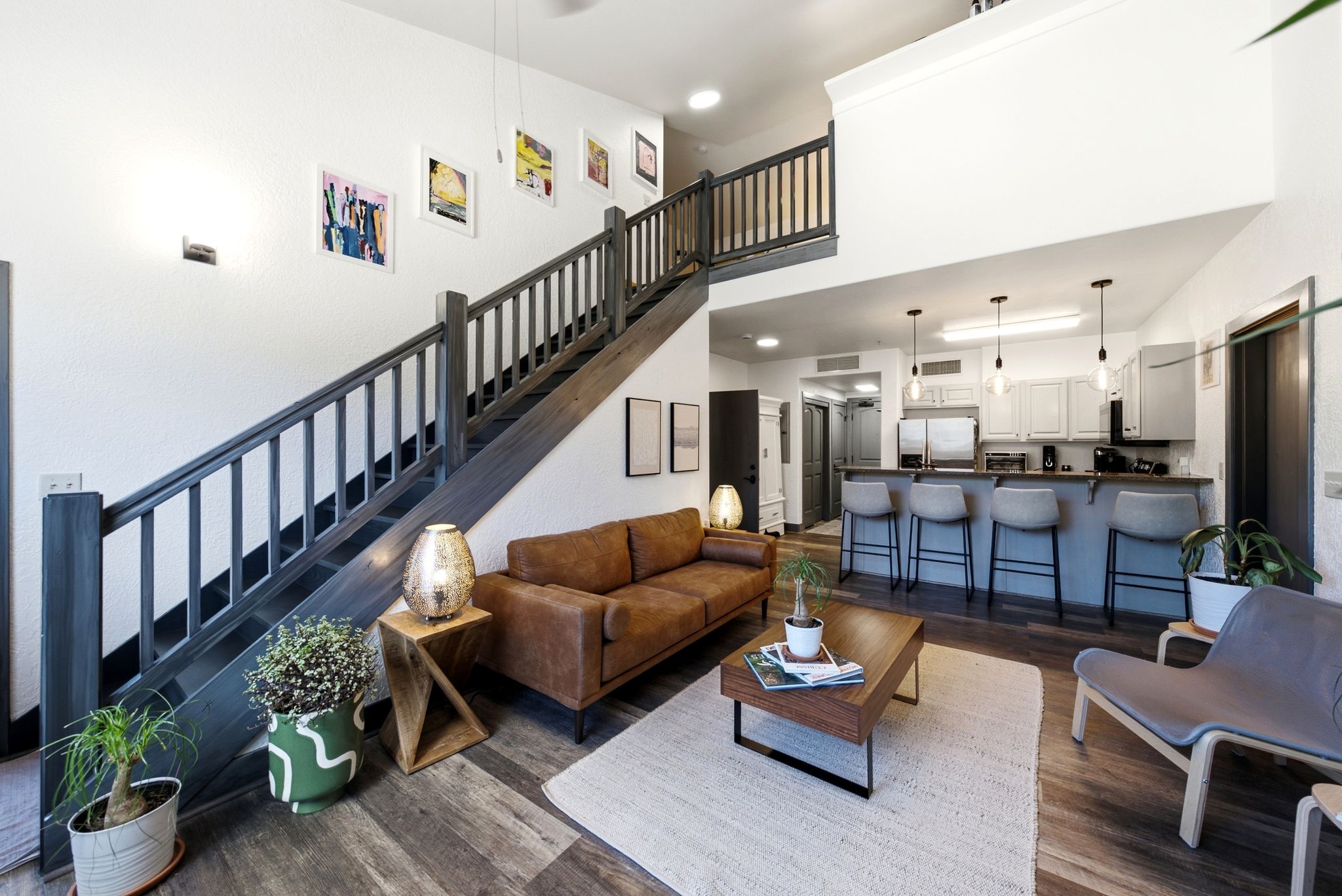 Open-concept living space featuring wood-finish flooring, a contemporary staircase with dark wood railing, and a kitchen island with built-in seating