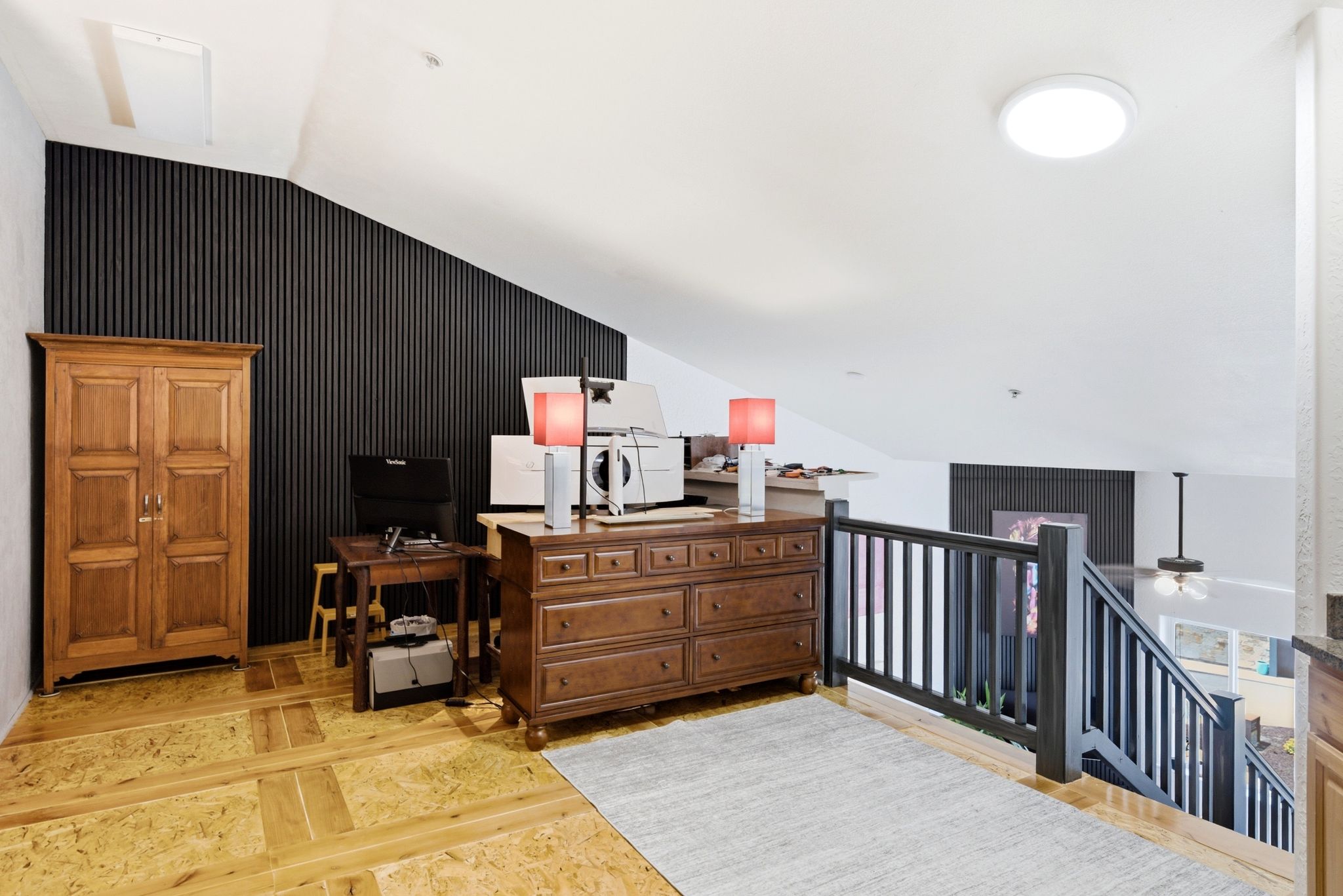 Upper-level landing featuring wood-finish flooring, a contemporary black slatted accent wall, and a dark wood-finish staircase railing