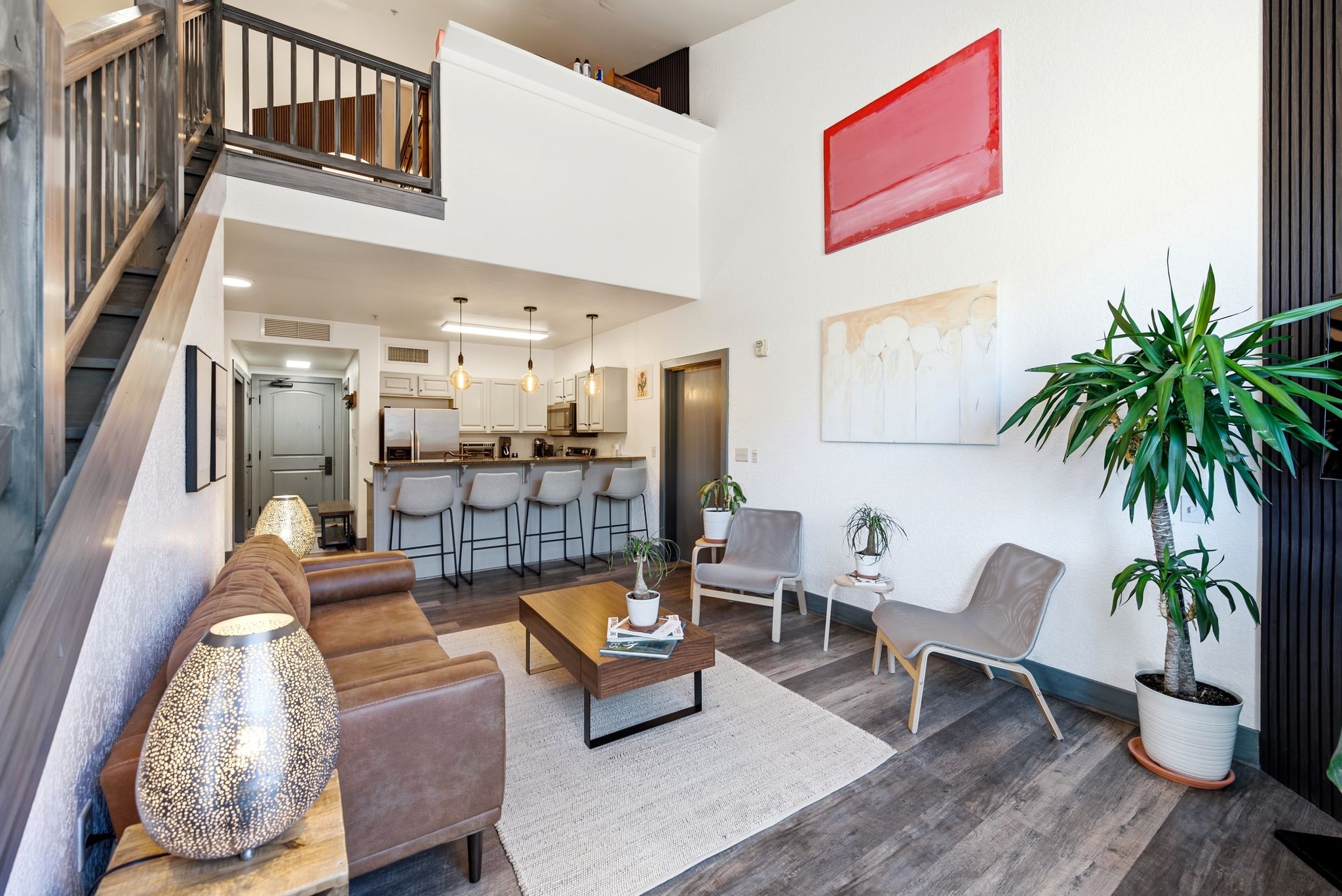 Open-concept living area featuring high ceilings, wood-finish flooring, a contemporary kitchen with light cabinetry, a built-in breakfast bar, and an overhead loft with a wooden railing