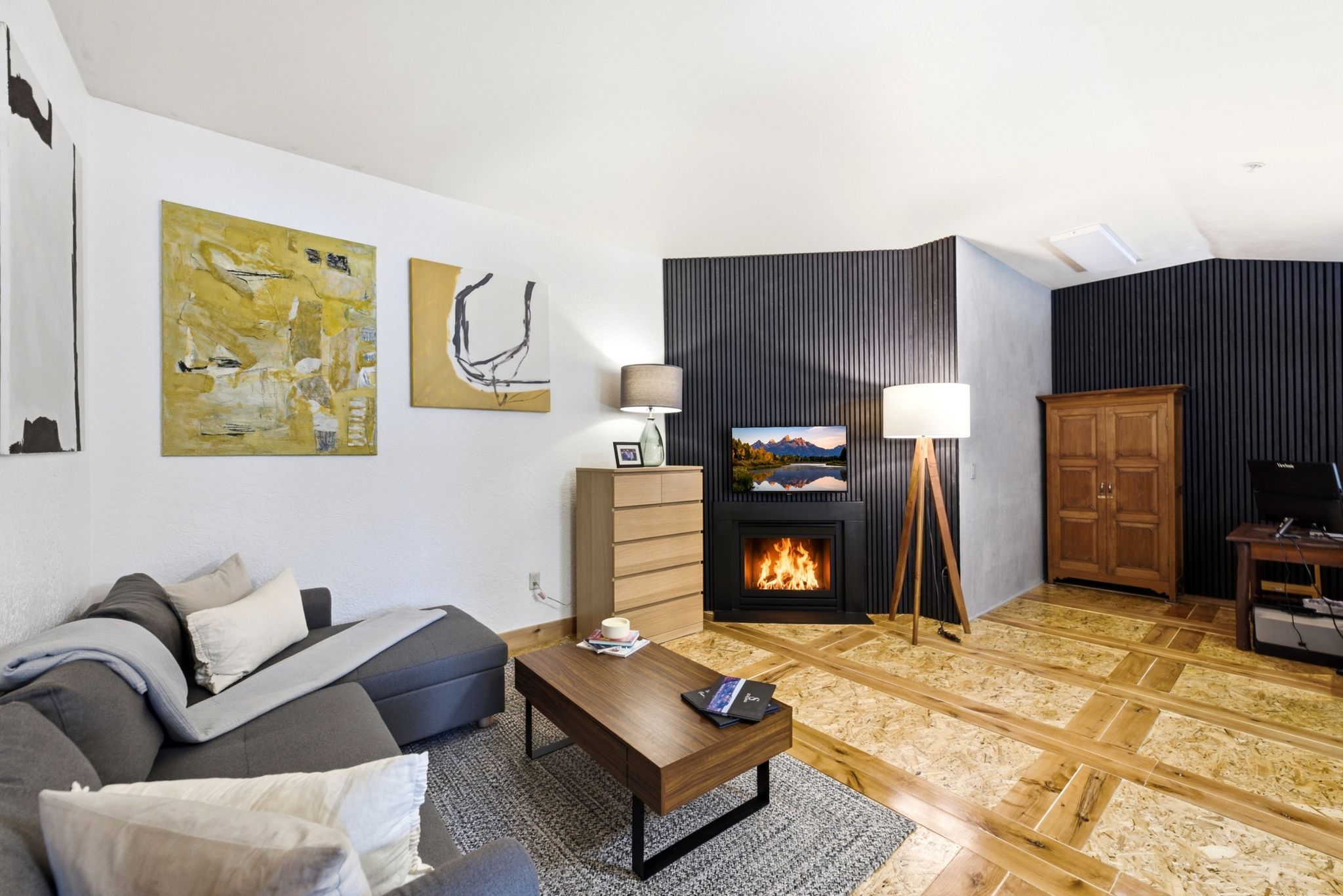 Living area featuring a floor-mounted fireplace, dark fluted accent walls, light wood-finish flooring, white walls, and a recessed ceiling light