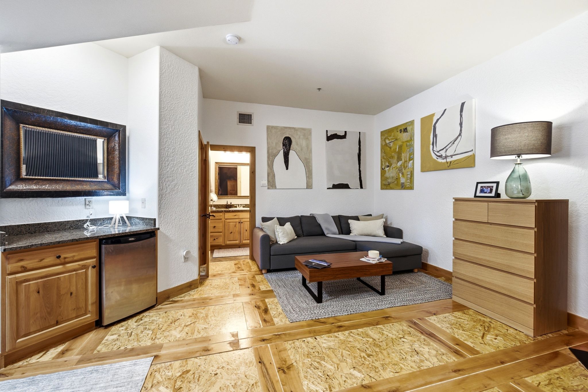 Living area featuring patterned wood-finish flooring, white textured walls, and a built-in wet bar with a stone countertop and stainless steel compact refrigerator