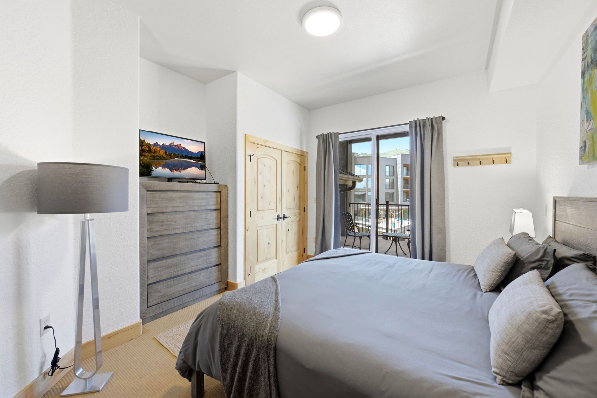 Bedroom featuring a private balcony with sliding glass doors, light wood-finish flooring, two natural wood-paneled doors, and a ceiling-mounted flush light fixture