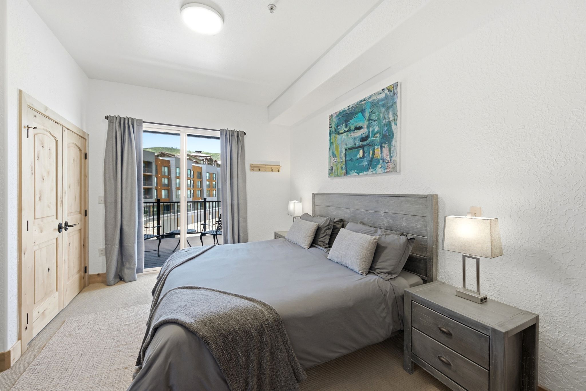 Bedroom featuring light-colored wood panel doors with black hardware, a balcony with black wrought iron railing, and carpeting