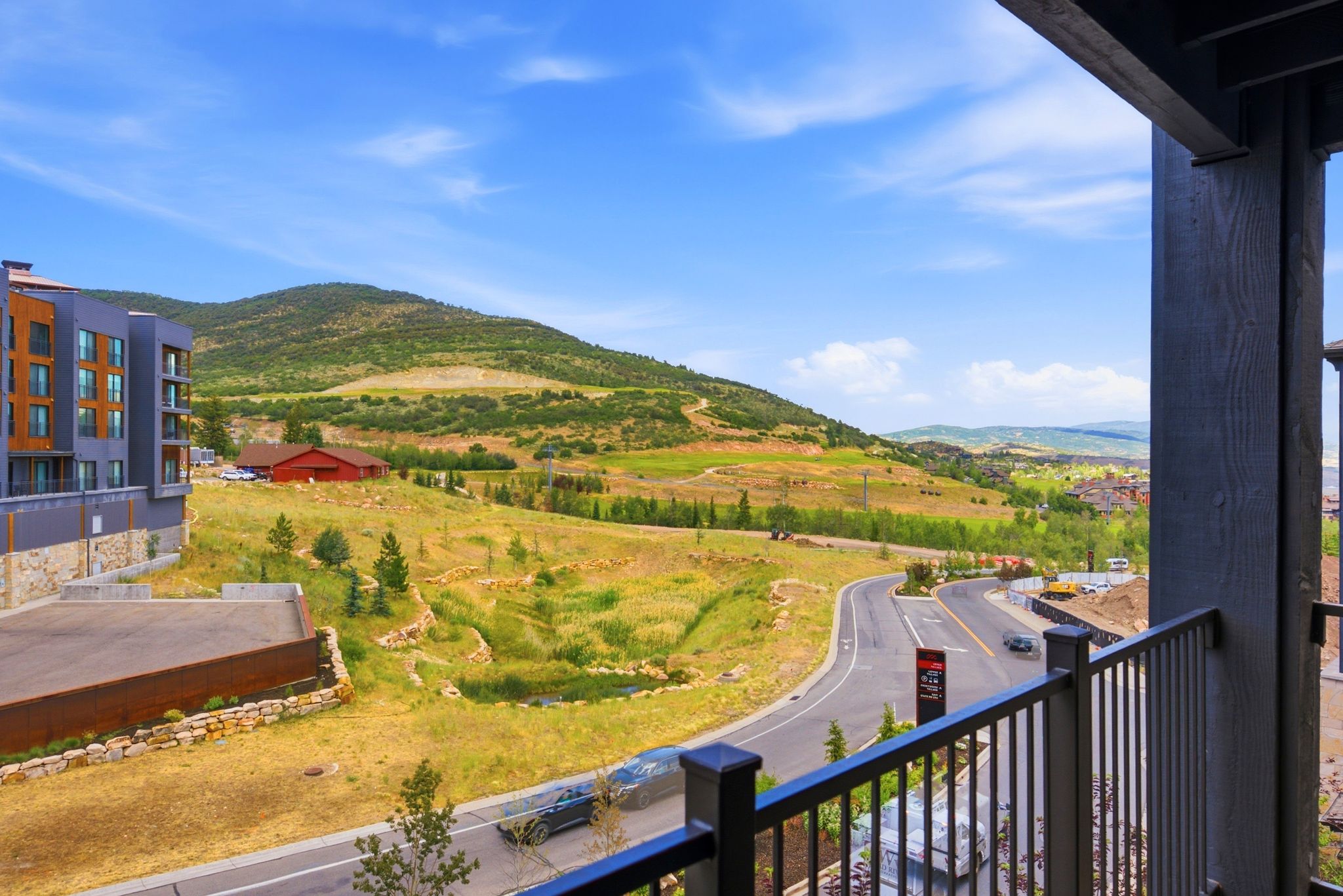 Mountainous landscape with expansive natural terrain, featuring a paved road, a pond, and a multi-story building