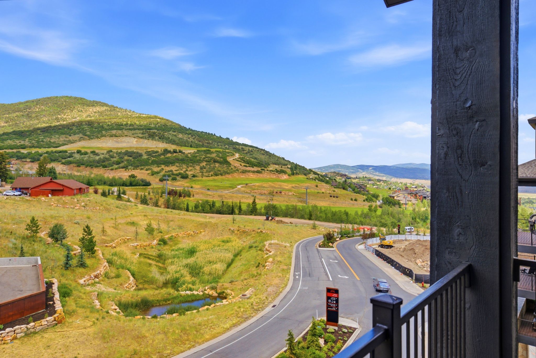 Expansive mountain and valley landscape with a paved road, natural rock retaining walls, and a small pond