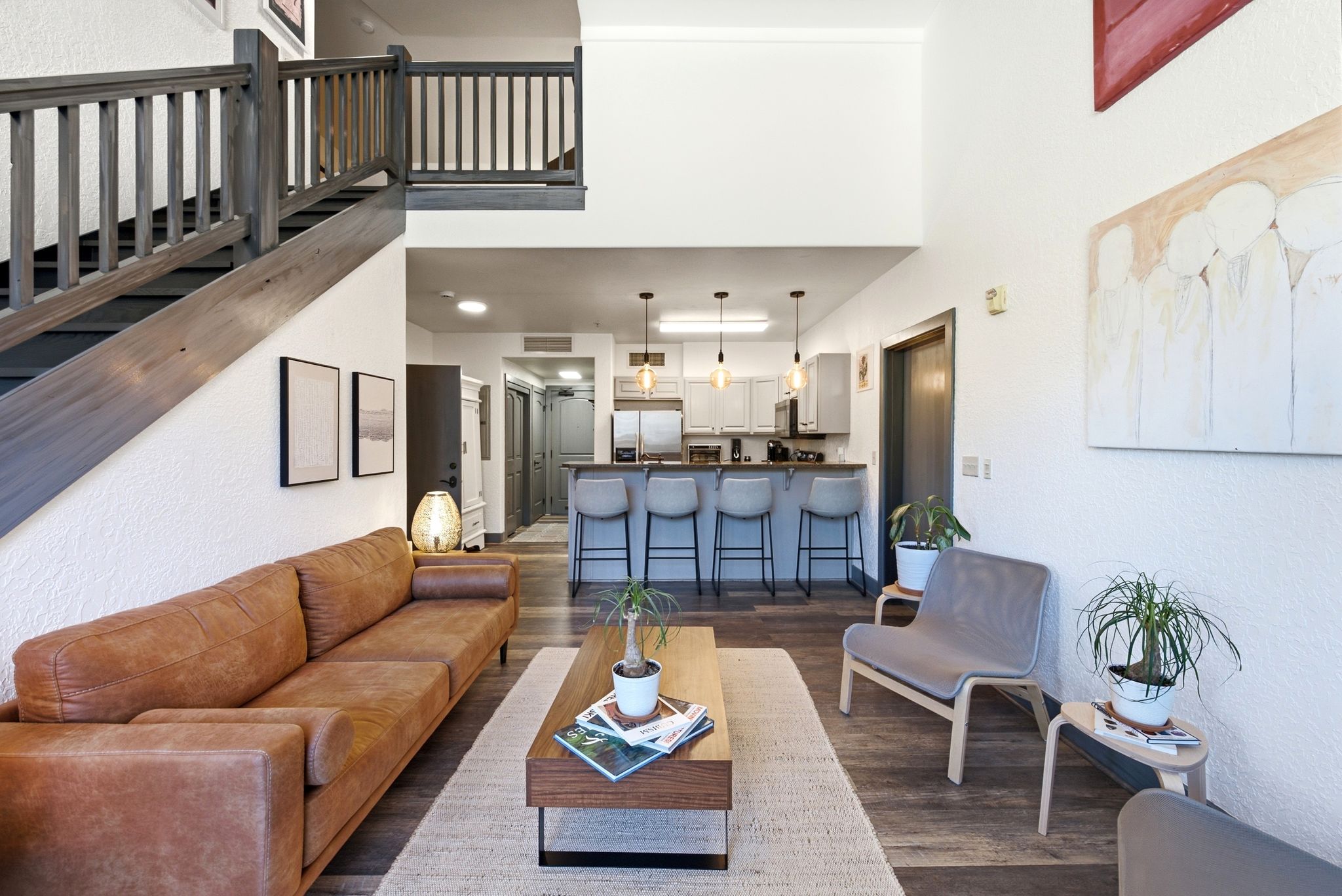 Open-concept living space featuring wood-finish flooring, a contemporary staircase with dark wood balusters, and high ceilings