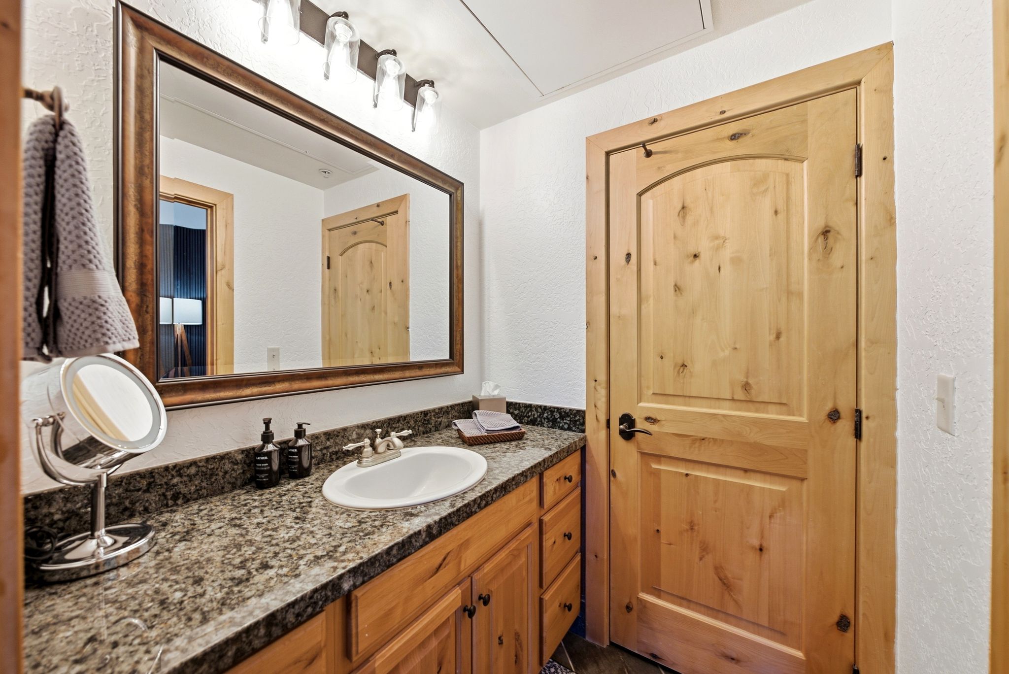 Bathroom featuring a natural wood vanity with an integrated sink, a granite-finish countertop, and a large framed mirror