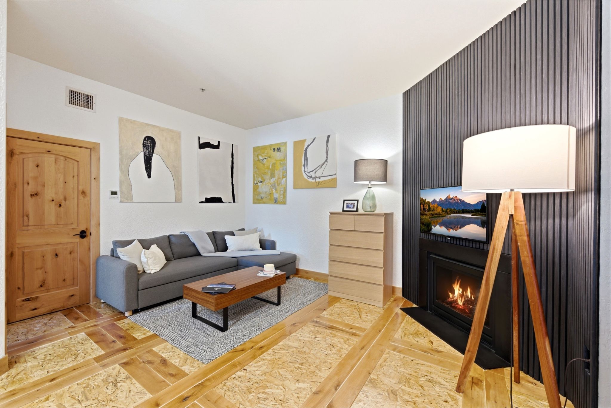 Living area featuring distinctive wood-finish flooring, a contemporary fireplace with a black surround, and a feature wall with vertical dark paneling