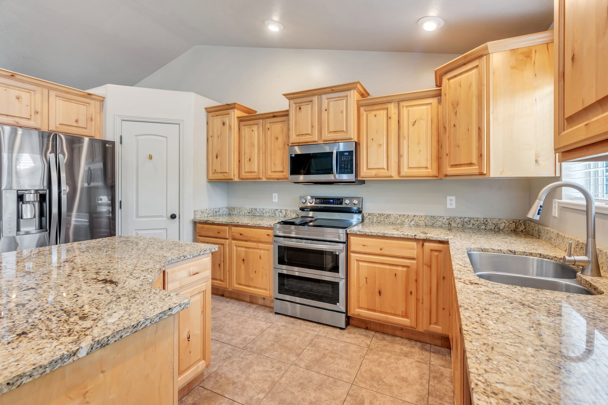 Kitchen featuring granite countertops, wood cabinetry, stainless steel appliances, a kitchen island, and tile flooring