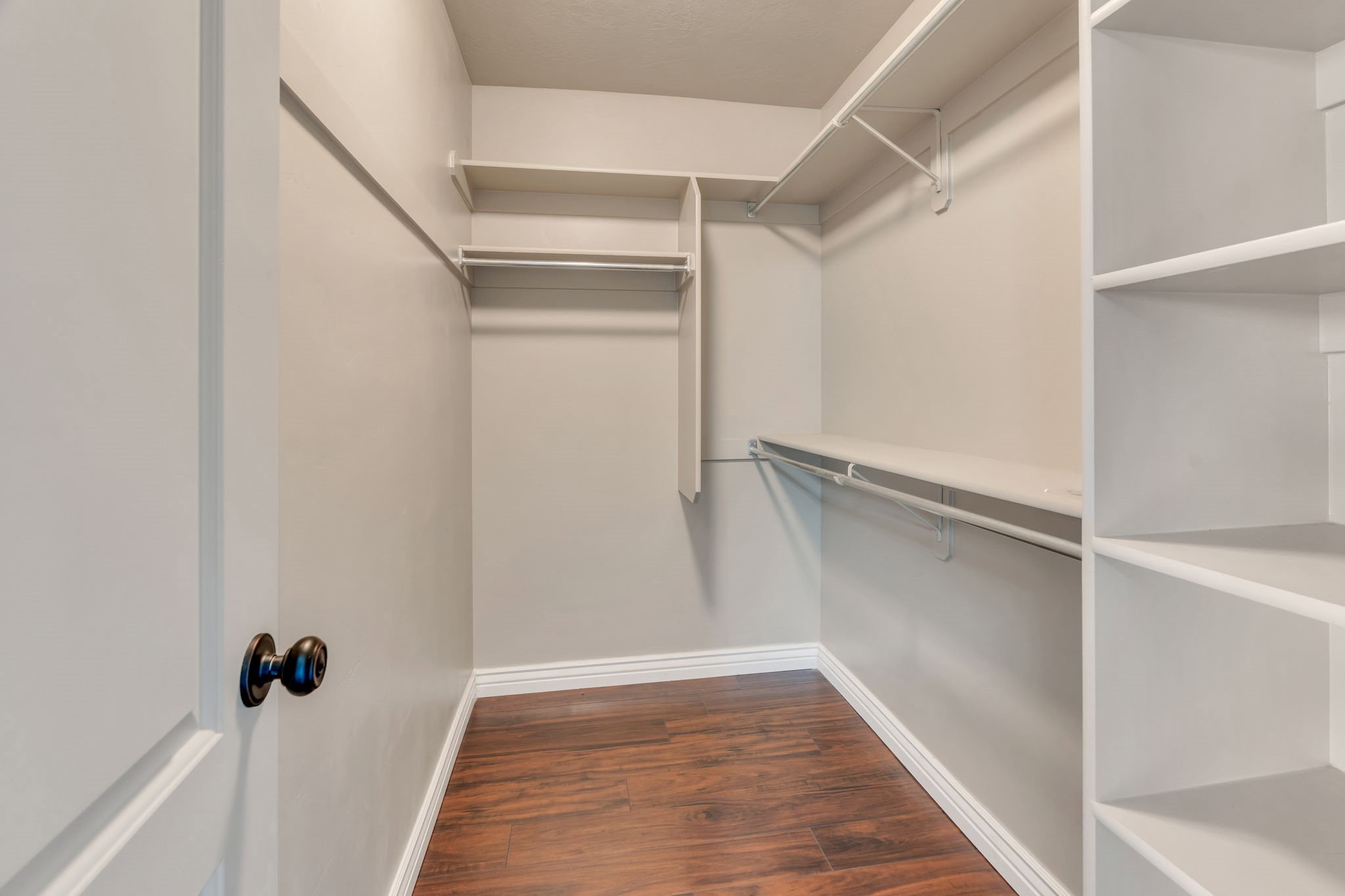 Walk-in closet featuring built-in shelving, multiple hanging rods, rich wood-finish flooring, and white baseboards