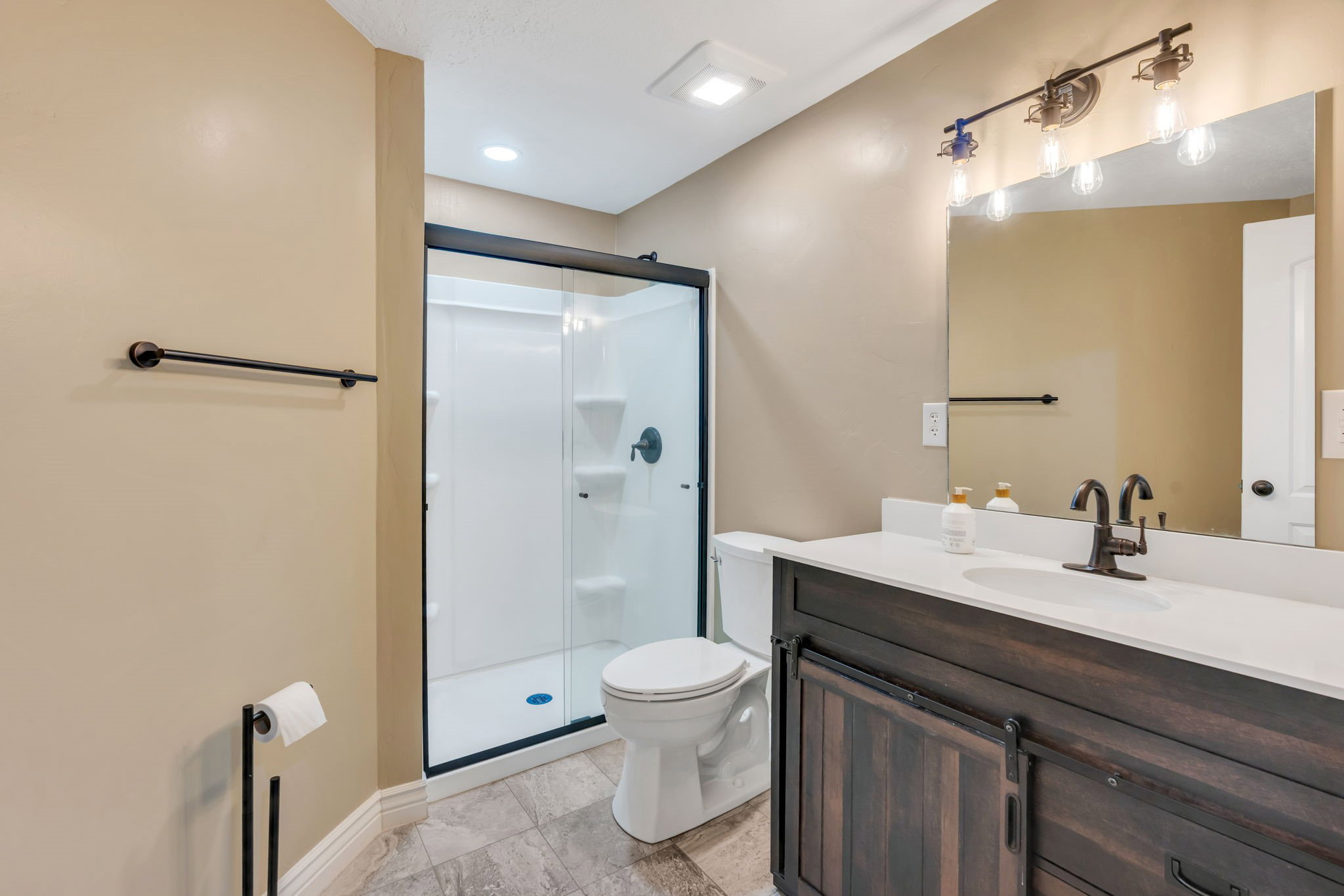 Full bathroom featuring a dark wood-finish vanity with a white countertop and undermount sink, a large wall-mounted mirror, and a shower with a black-framed glass enclosure