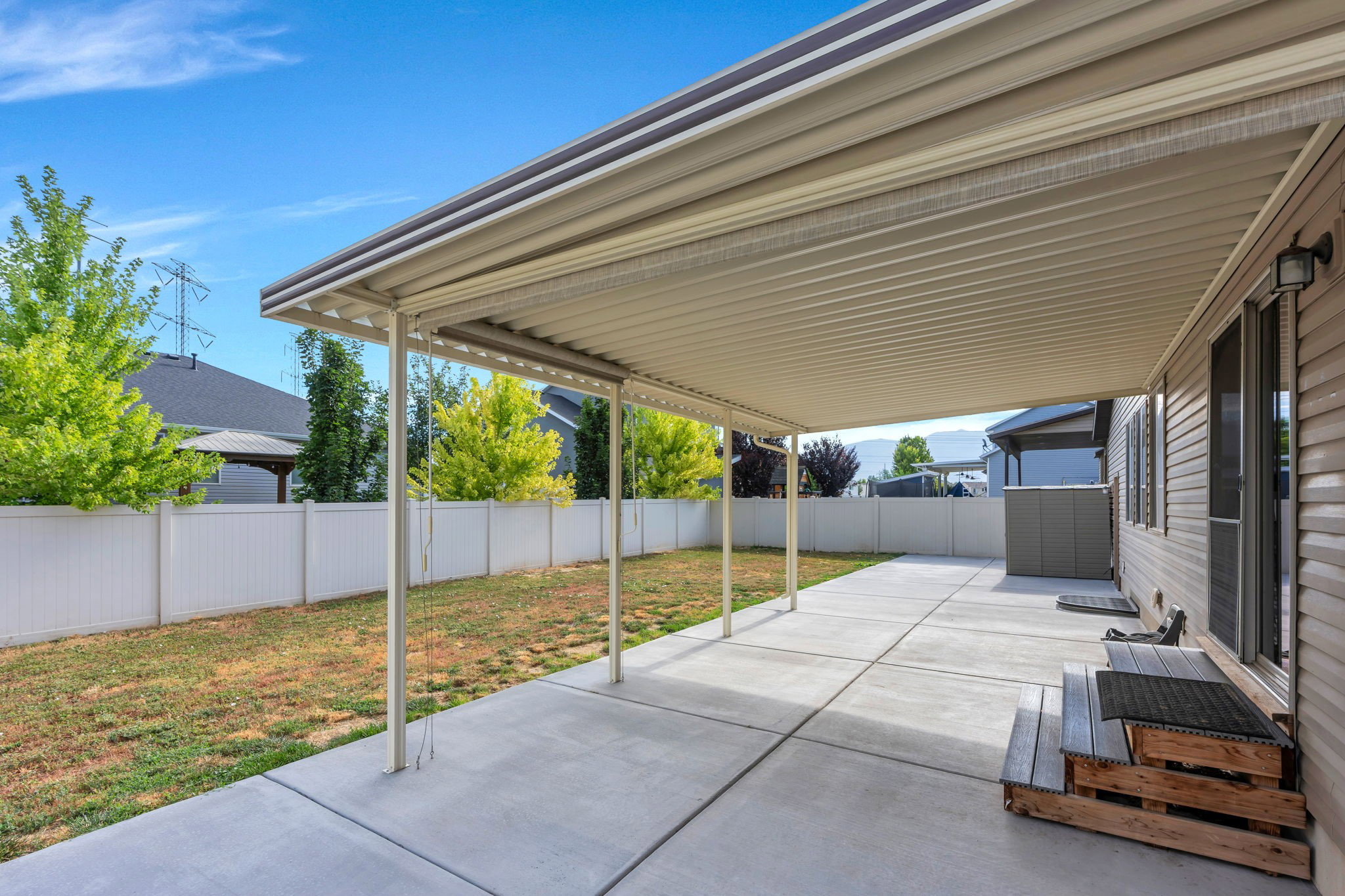 Expansive covered patio featuring a corrugated metal roof and supportive columns, extending over a concrete slab