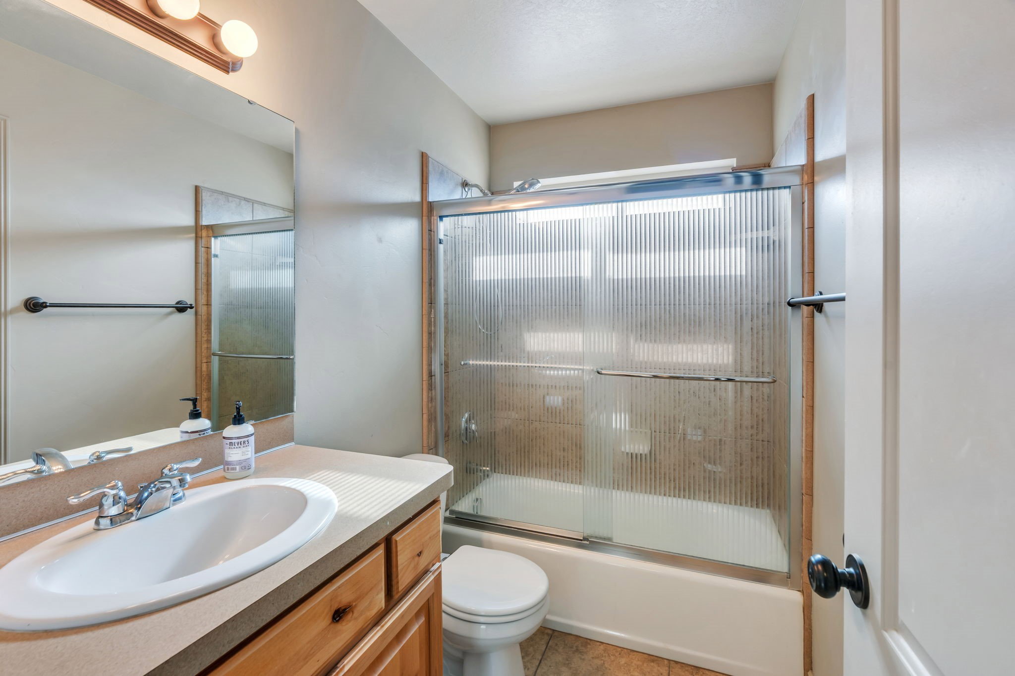 Bathroom featuring a single vanity with an integrated sink, wood-finish cabinetry, and a full-width mirror
