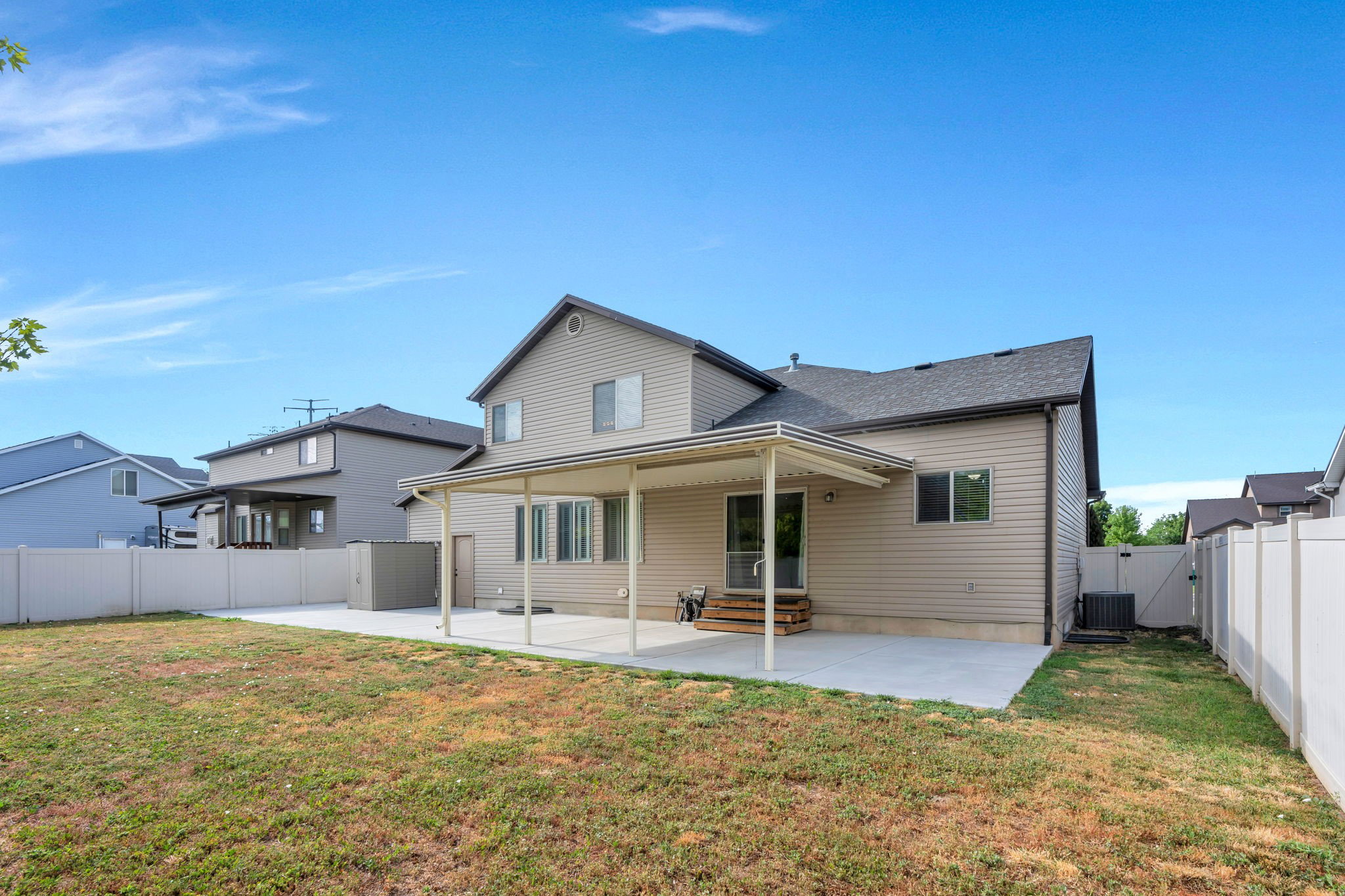 Expansive backyard featuring a covered patio, a large concrete pad, vinyl privacy fencing, and a built-in outdoor storage shed
