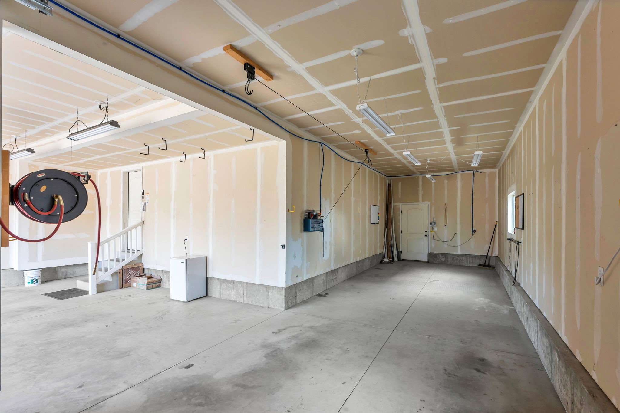 Expansive concrete floor garage space with fluorescent lighting, partial drywall, and multiple utility access points