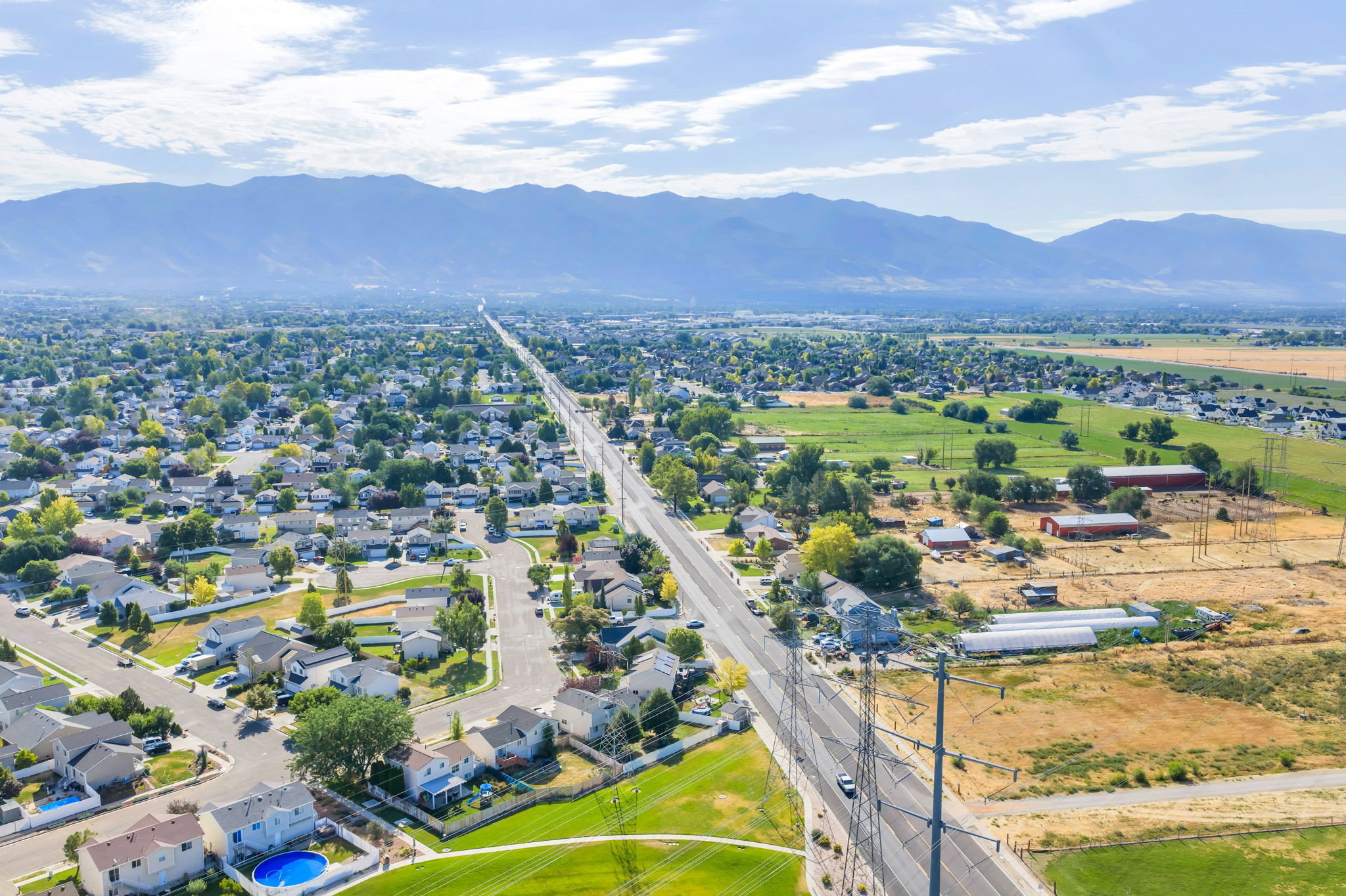 Expansive aerial perspective showcasing a residential development with established homes, green spaces, and a prominent roadway