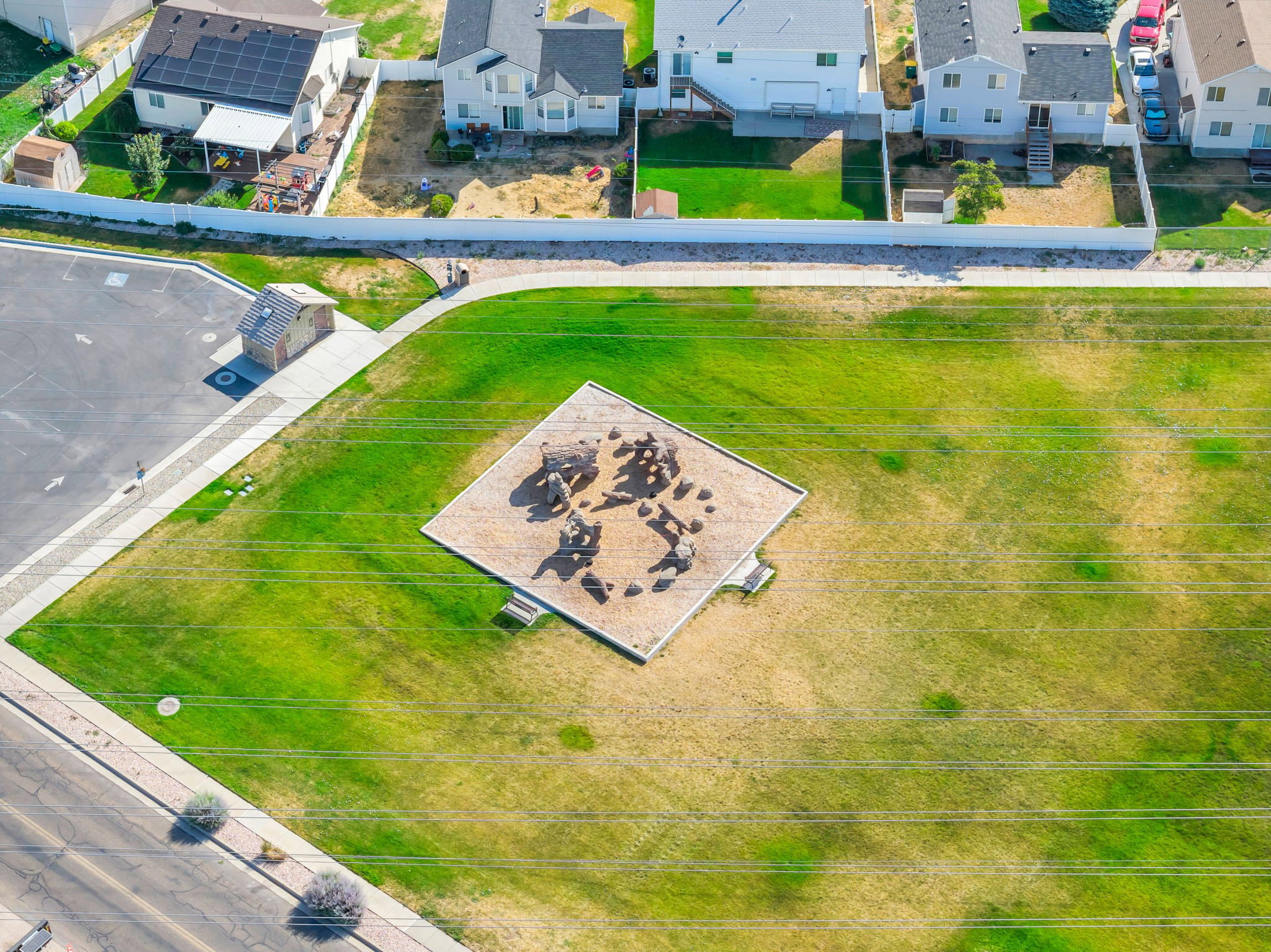 Expansive green space featuring a dedicated playground area with multiple structures, concrete sidewalks, and a paved street bordering the property