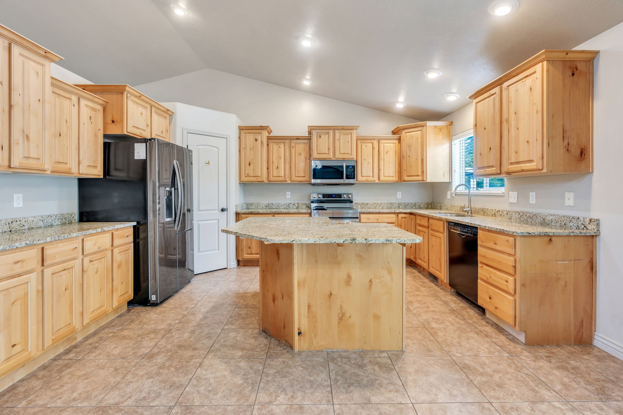 Spacious kitchen featuring light wood cabinetry, stone countertops, stainless steel appliances, and a central island with additional counter space