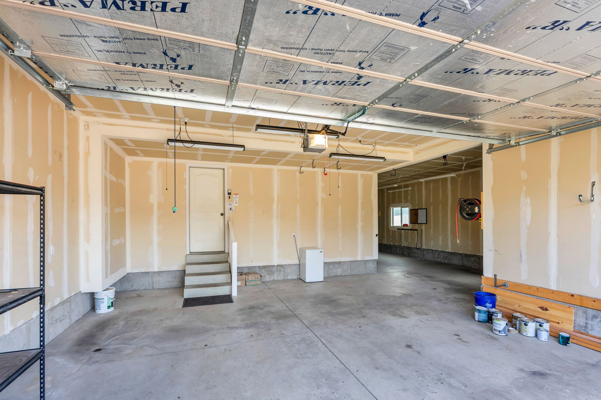 Spacious garage featuring a concrete floor, exposed joist ceiling with insulation, and unfinished drywall walls