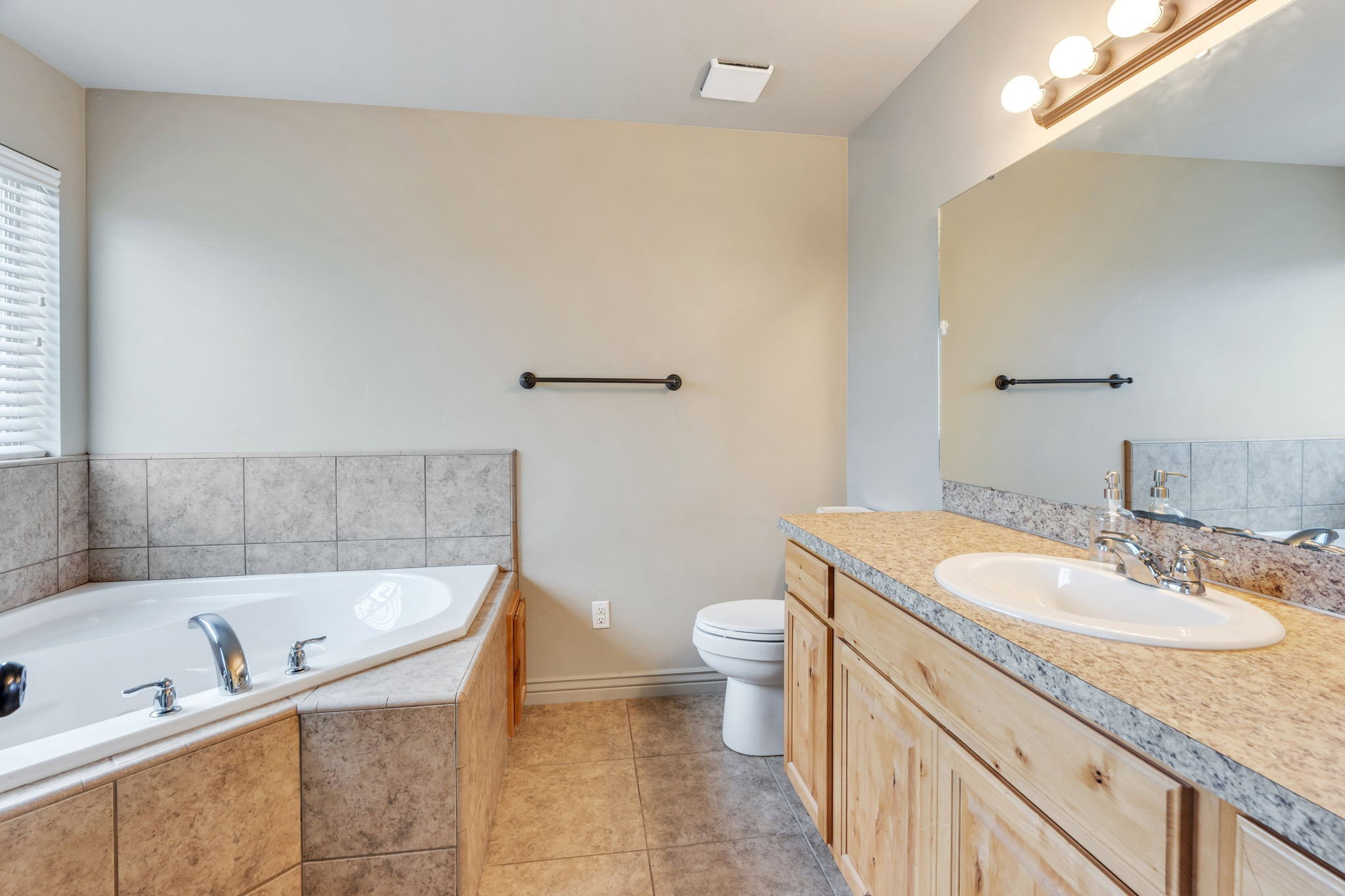 Bathroom featuring a corner soaking tub with tiled surround, a single vanity with an integrated sink and light wood cabinetry, a light-toned countertop, and a vanity mirror