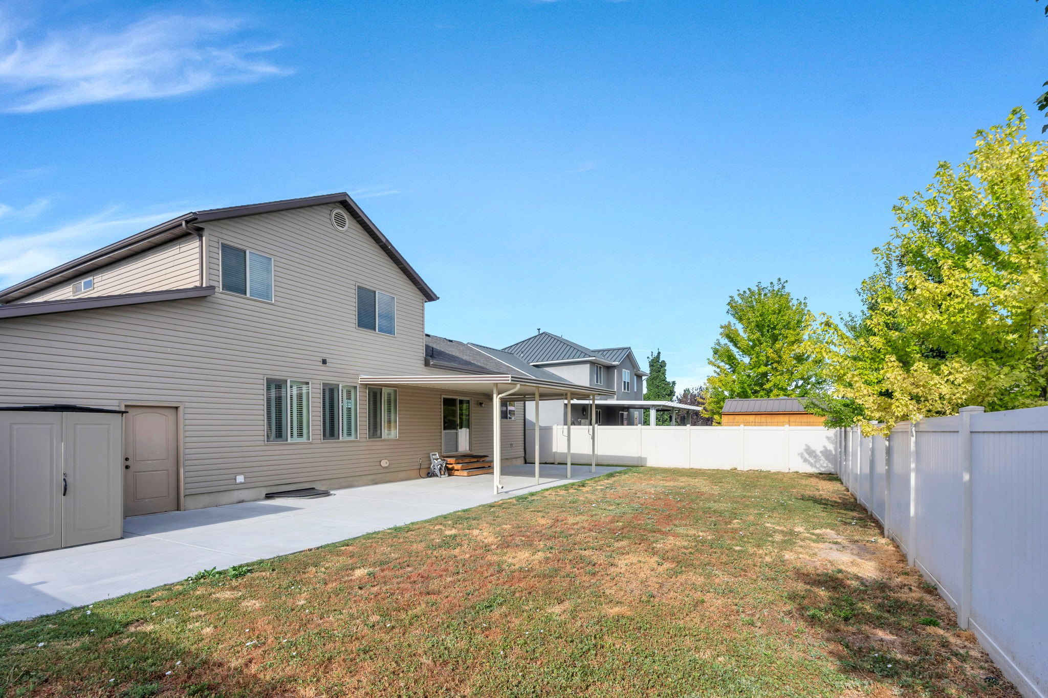 Spacious backyard featuring a covered patio, concrete pathway, and a privacy fence