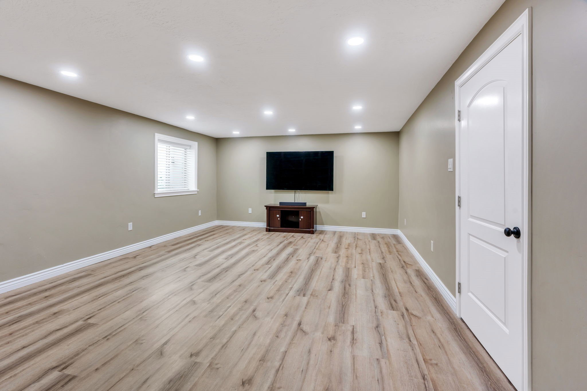 Spacious room featuring wood-finish flooring, recessed lighting, and a white interior door with a black knob