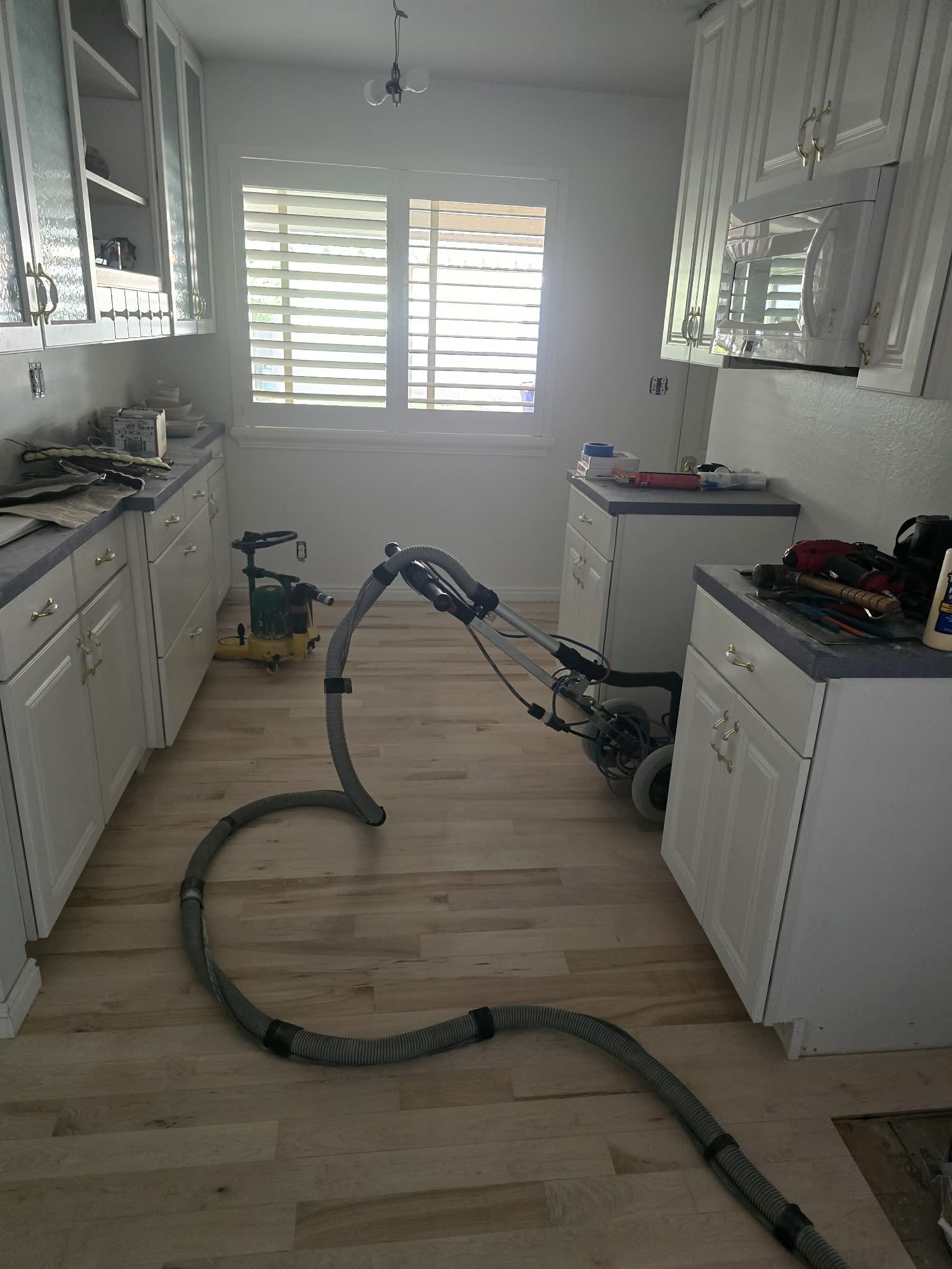 Kitchen featuring light-toned wood-finish flooring, white cabinetry with gold-toned hardware, and a window with white louvered shutters