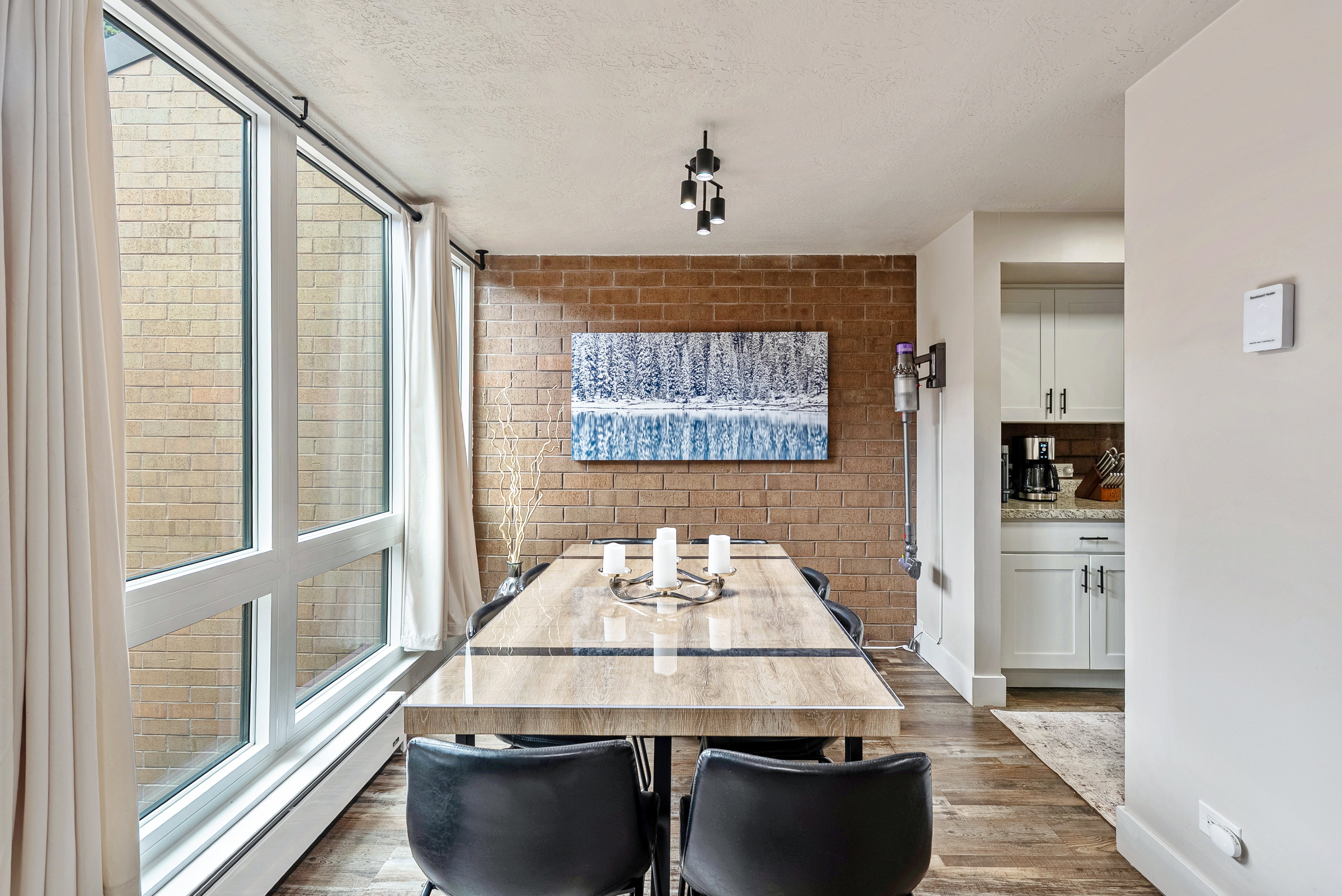 Dining area featuring a full-height window, exposed brick accent wall, wood-finish flooring, and track lighting